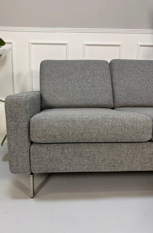 Gebrauchtes graues COR Conseta Designer Stoff Sofa vor einer Wand, stilvoll und modern eingerichtet.