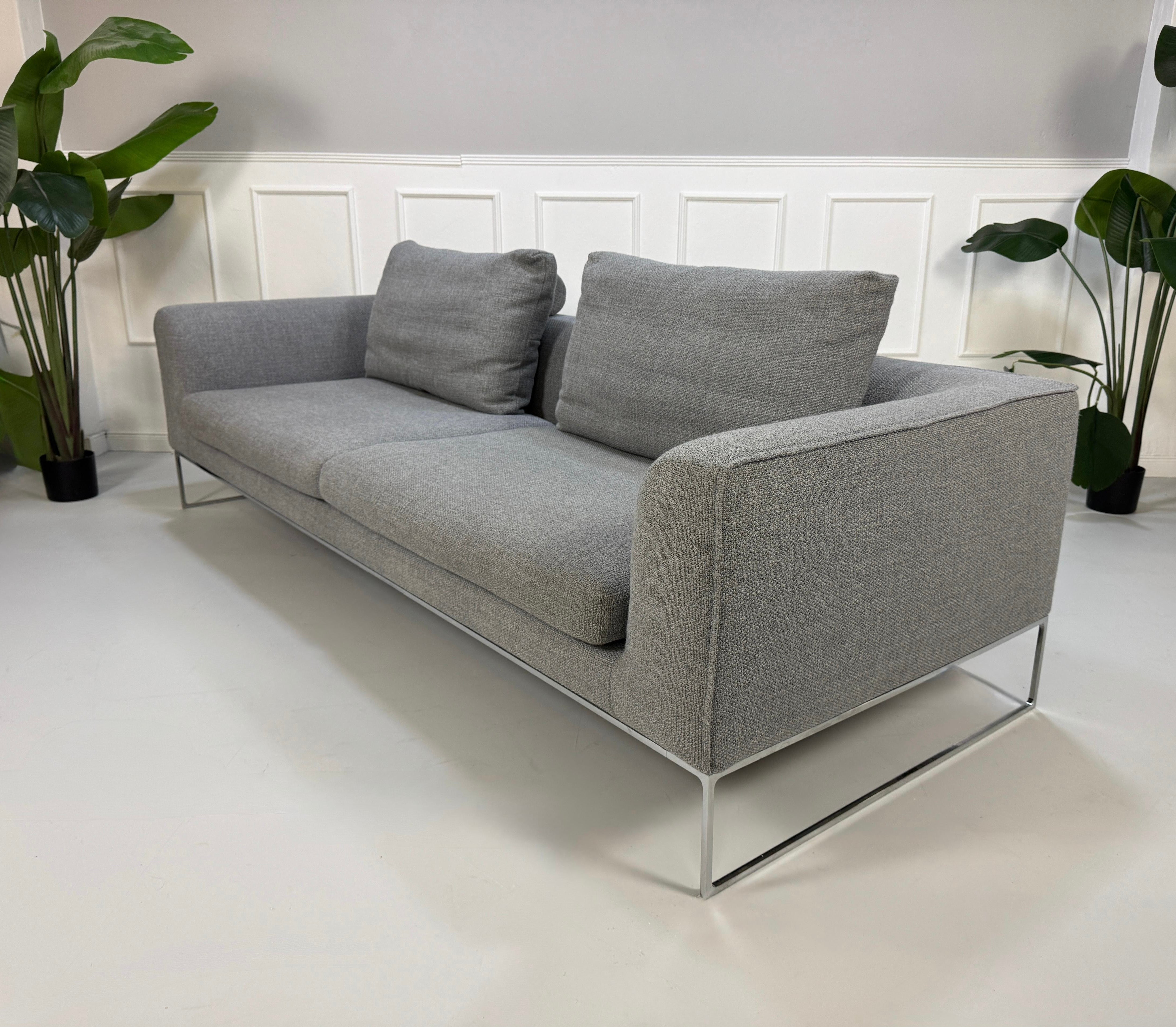Erneuertes graues COR Mell Designer Stoff Sofa vor einer Wand, stilvoll und modern eingerichtet.
