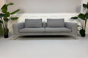 Erneuertes graues COR Mell Designer Stoff Sofa vor einer Wand, stilvoll und modern eingerichtet.