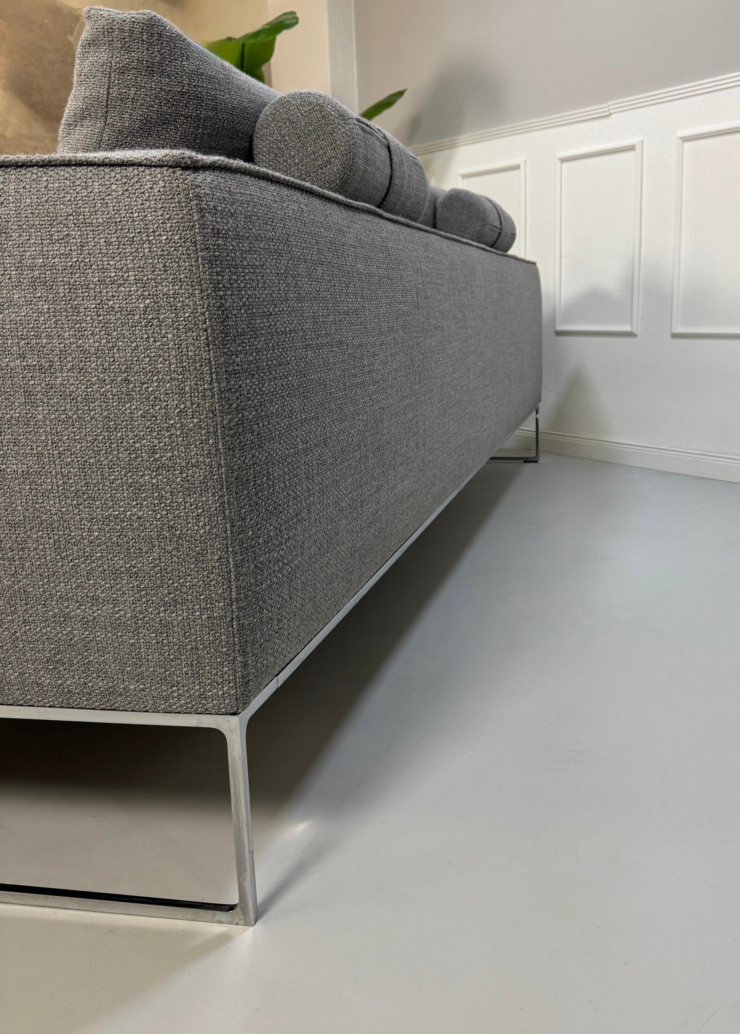Erneuertes graues COR Mell Designer Stoff Sofa vor einer Wand, stilvoll und modern eingerichtet.