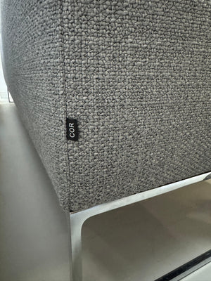 Erneuertes graues COR Mell Designer Stoff Sofa vor einer Wand, stilvoll und modern eingerichtet.