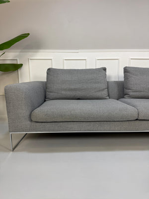 Erneuertes graues COR Mell Designer Stoff Sofa vor einer Wand, stilvoll und modern eingerichtet.