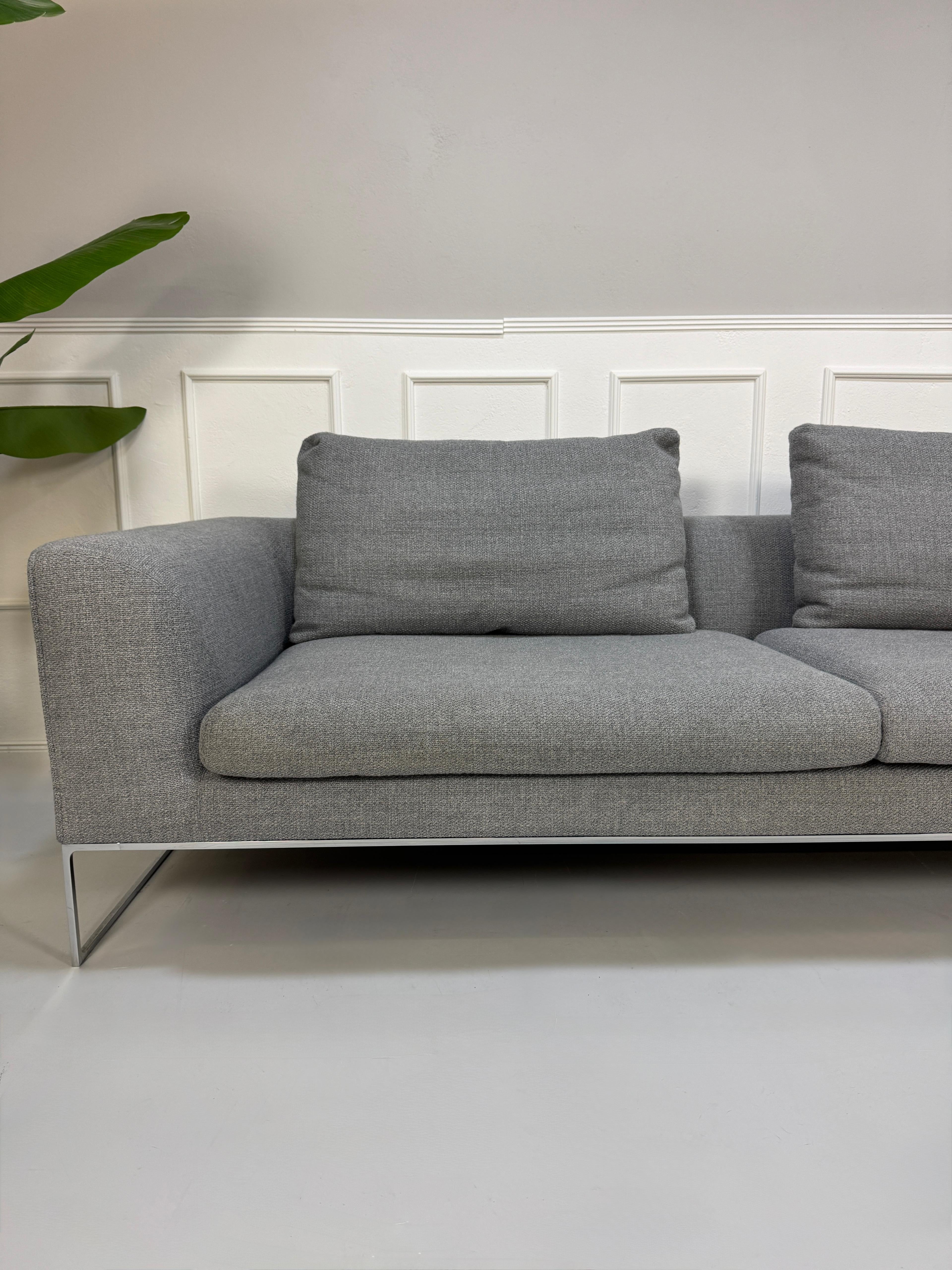 Erneuertes graues COR Mell Designer Stoff Sofa vor einer Wand, stilvoll und modern eingerichtet.