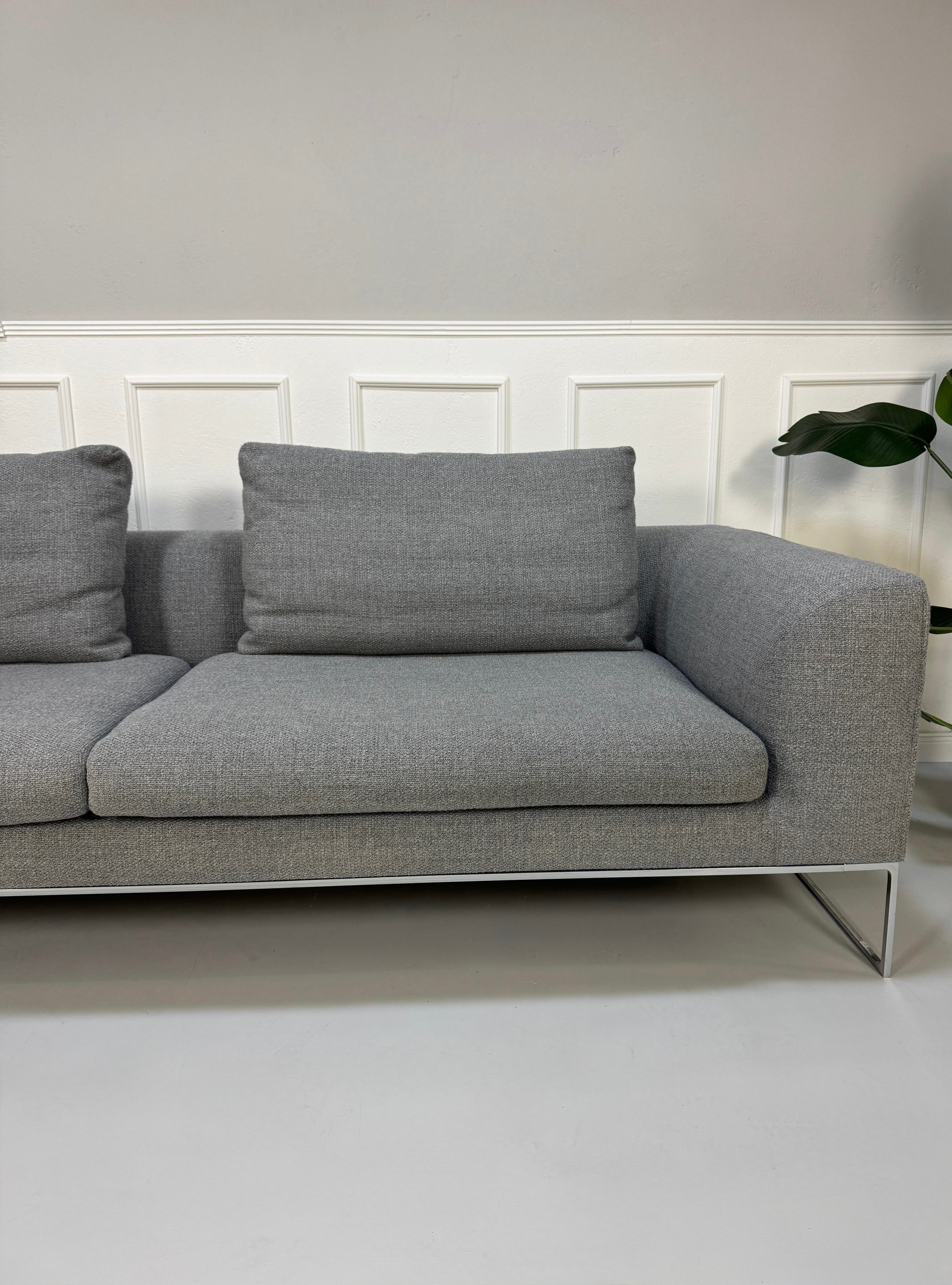 Erneuertes graues COR Mell Designer Stoff Sofa vor einer Wand, stilvoll und modern eingerichtet.