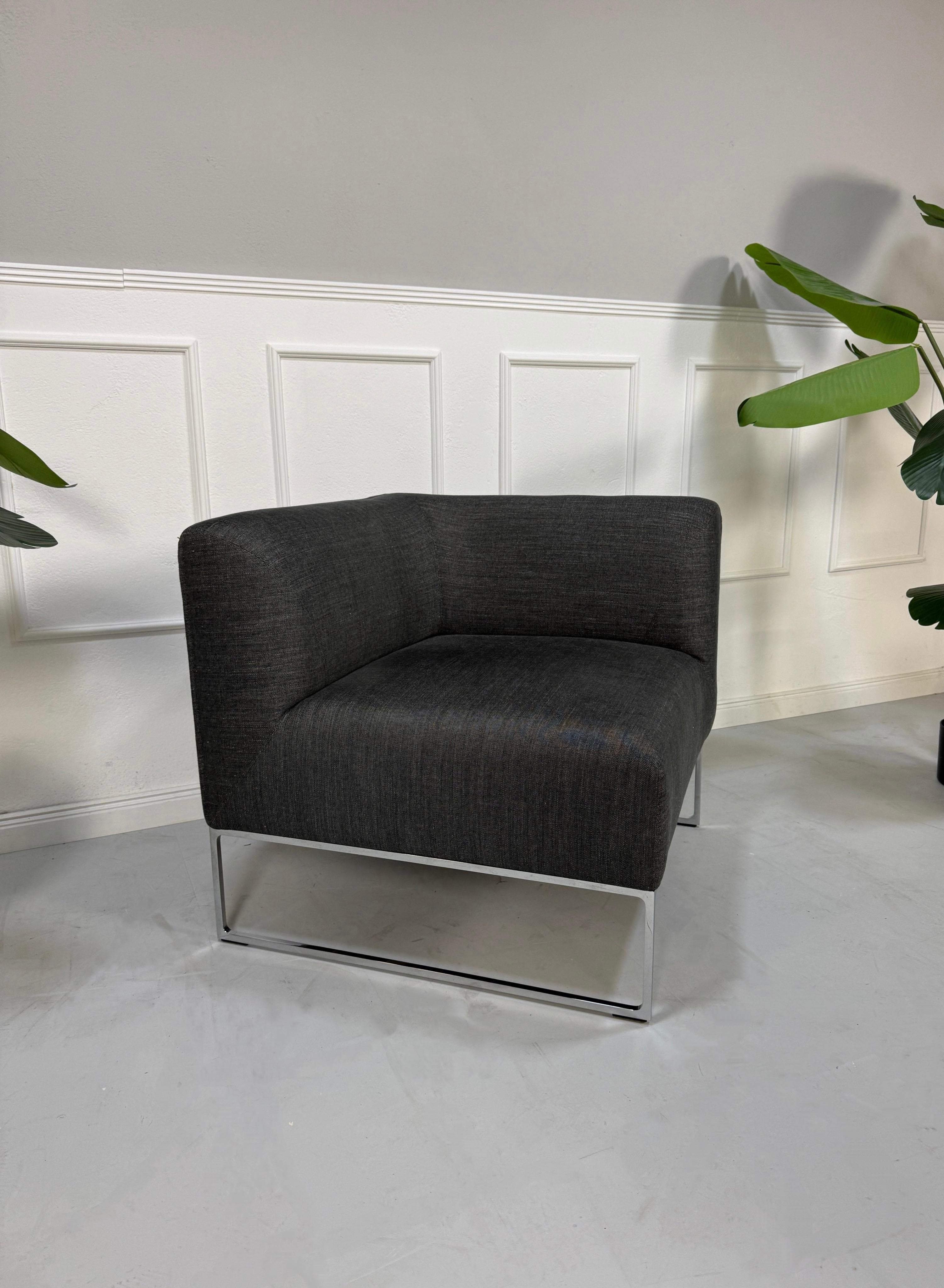 Gebrauchtes graues COR Mell Designer Stoff Sofa vor einer Wand, stilvoll und modern eingerichtet.