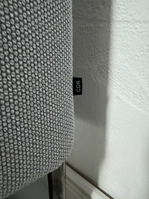 Gebrauchtes graues COR Pilotis Designer Stoff Sofa vor einer Wand, stilvoll und modern eingerichtet.