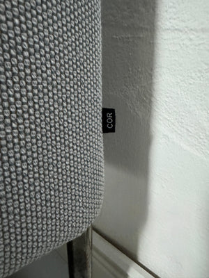 Gebrauchtes graues COR Pilotis Designer Stoff Sofa vor einer Wand, stilvoll und modern eingerichtet.