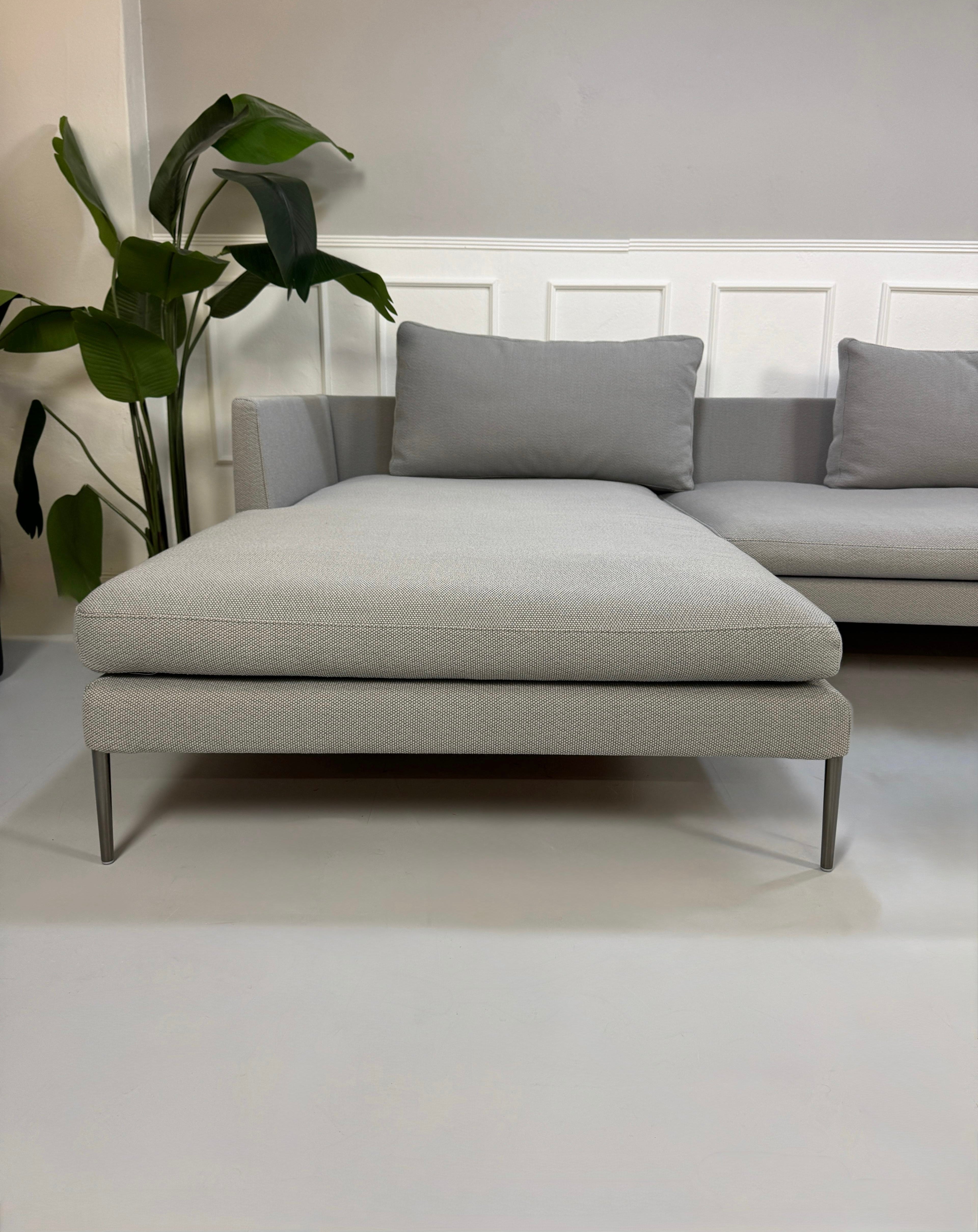 Gebrauchtes graues COR Pilotis Designer Stoff Sofa vor einer Wand, stilvoll und modern eingerichtet.