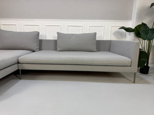 Gebrauchtes graues COR Pilotis Designer Stoff Sofa vor einer Wand, stilvoll und modern eingerichtet.