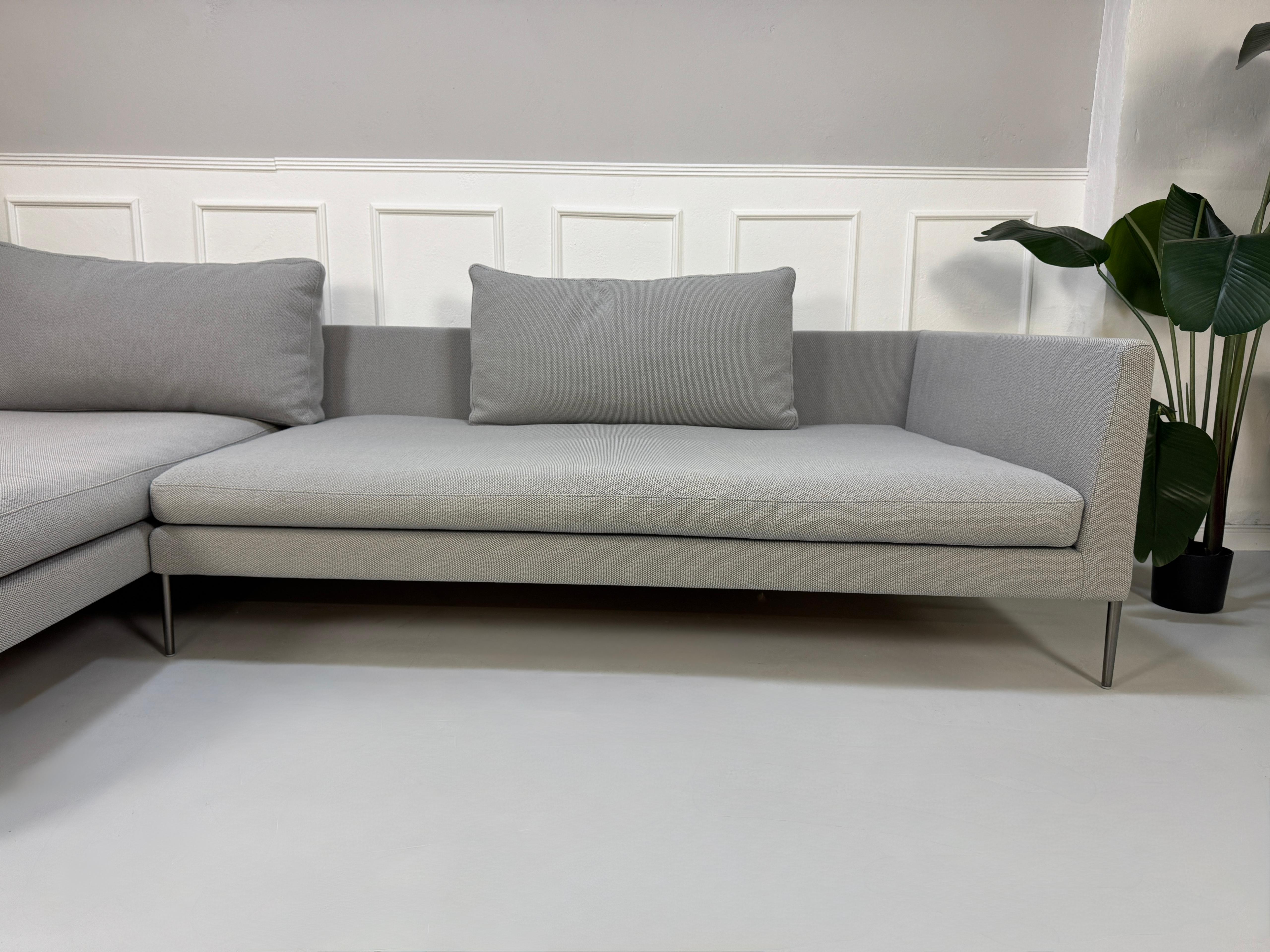 Gebrauchtes graues COR Pilotis Designer Stoff Sofa vor einer Wand, stilvoll und modern eingerichtet.