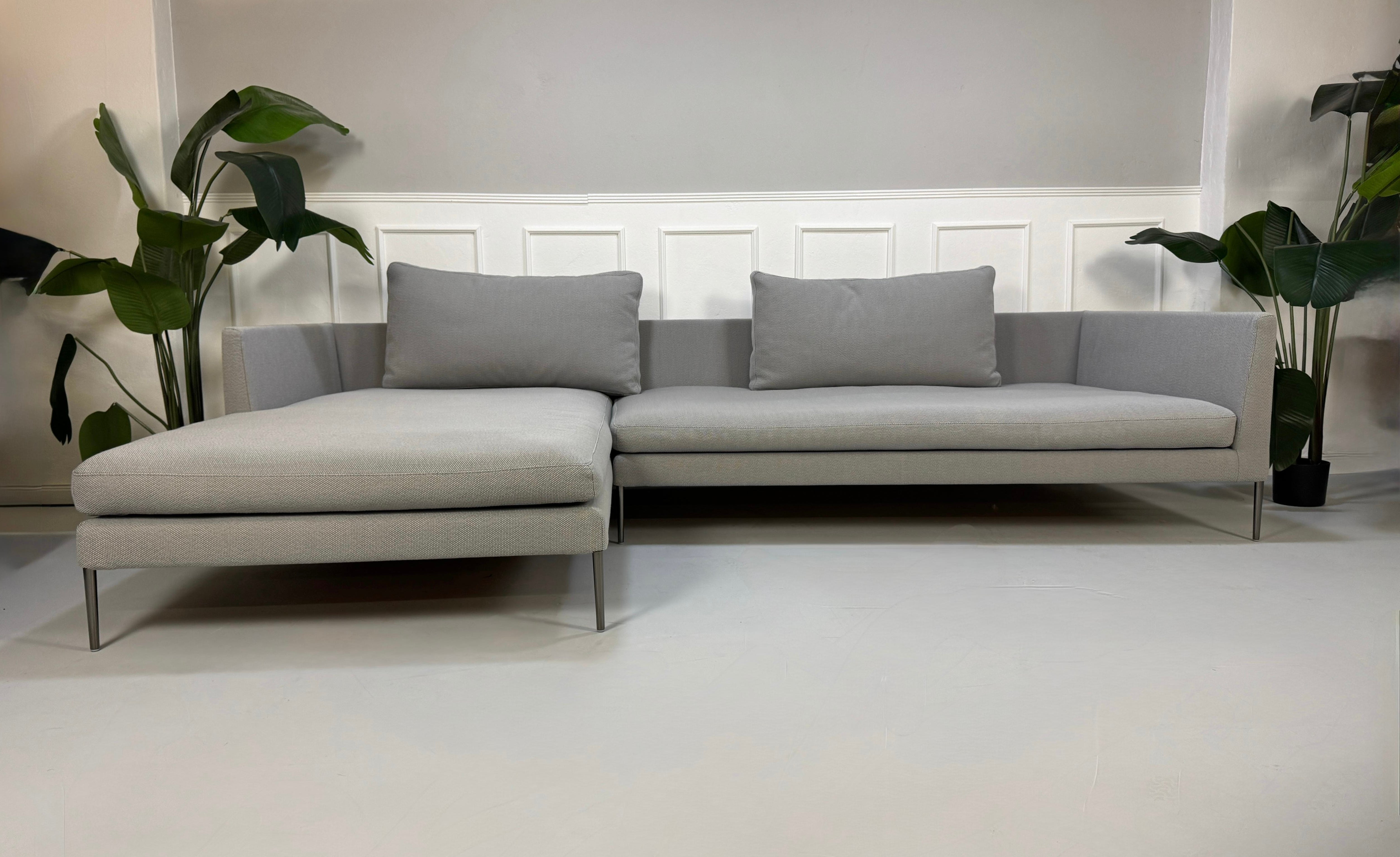 Gebrauchtes graues COR Pilotis Designer Stoff Sofa vor einer Wand, stilvoll und modern eingerichtet.