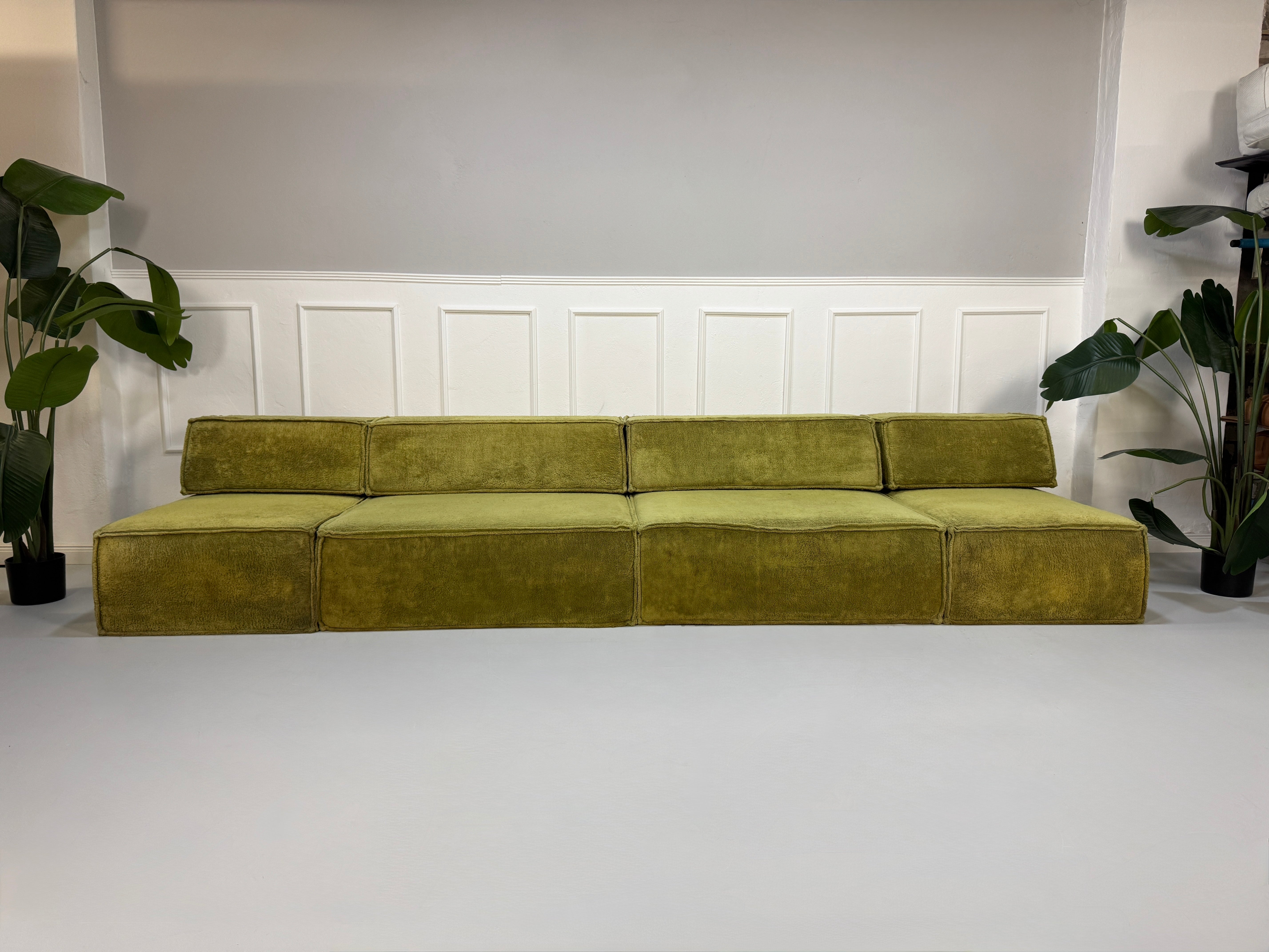 Gebrauchtes grünes Stoffsofa COR Modell Trio vor einer modernen Wand.