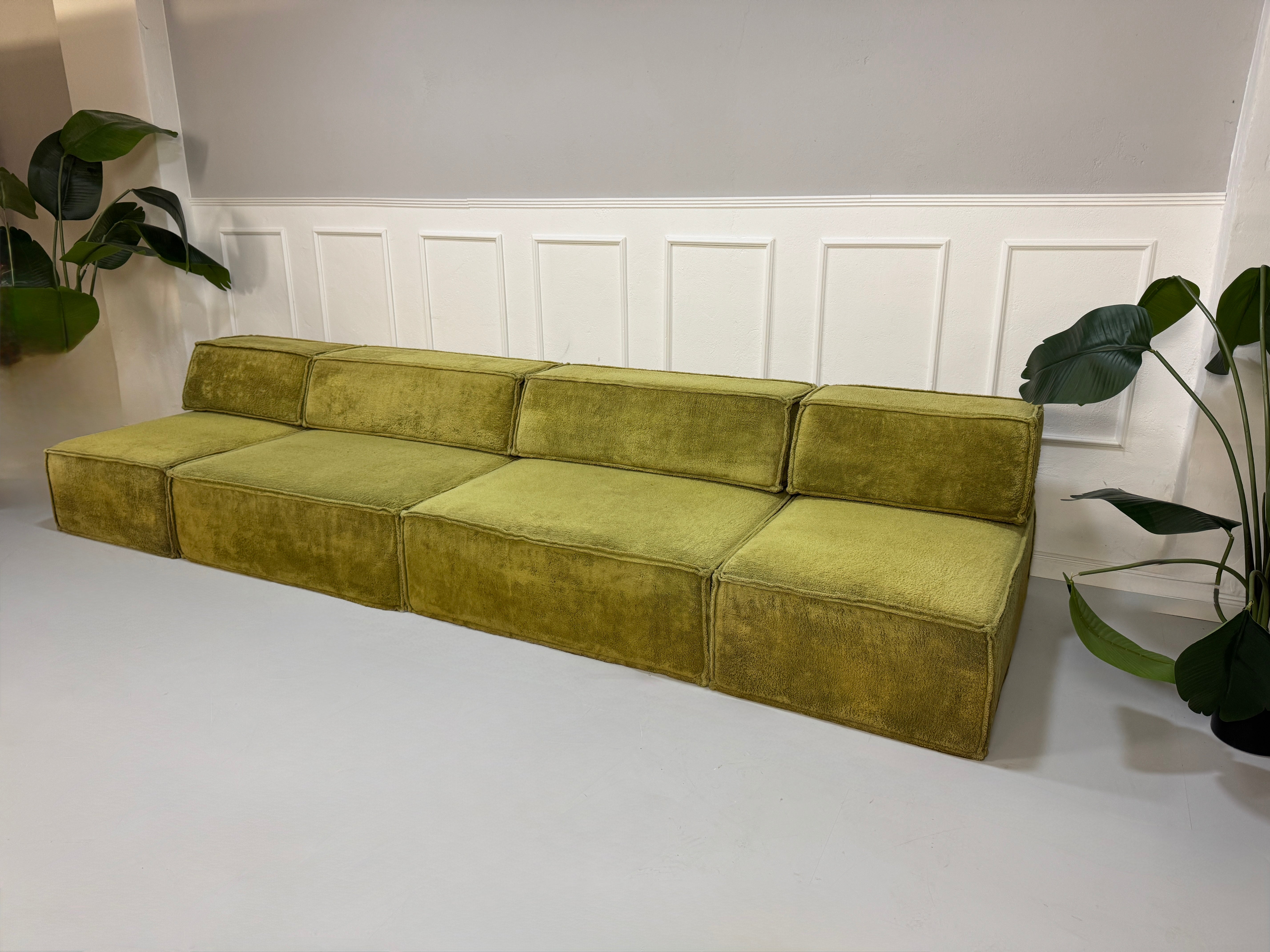 Gebrauchtes grünes Stoffsofa COR Modell Trio vor einer modernen Wand.