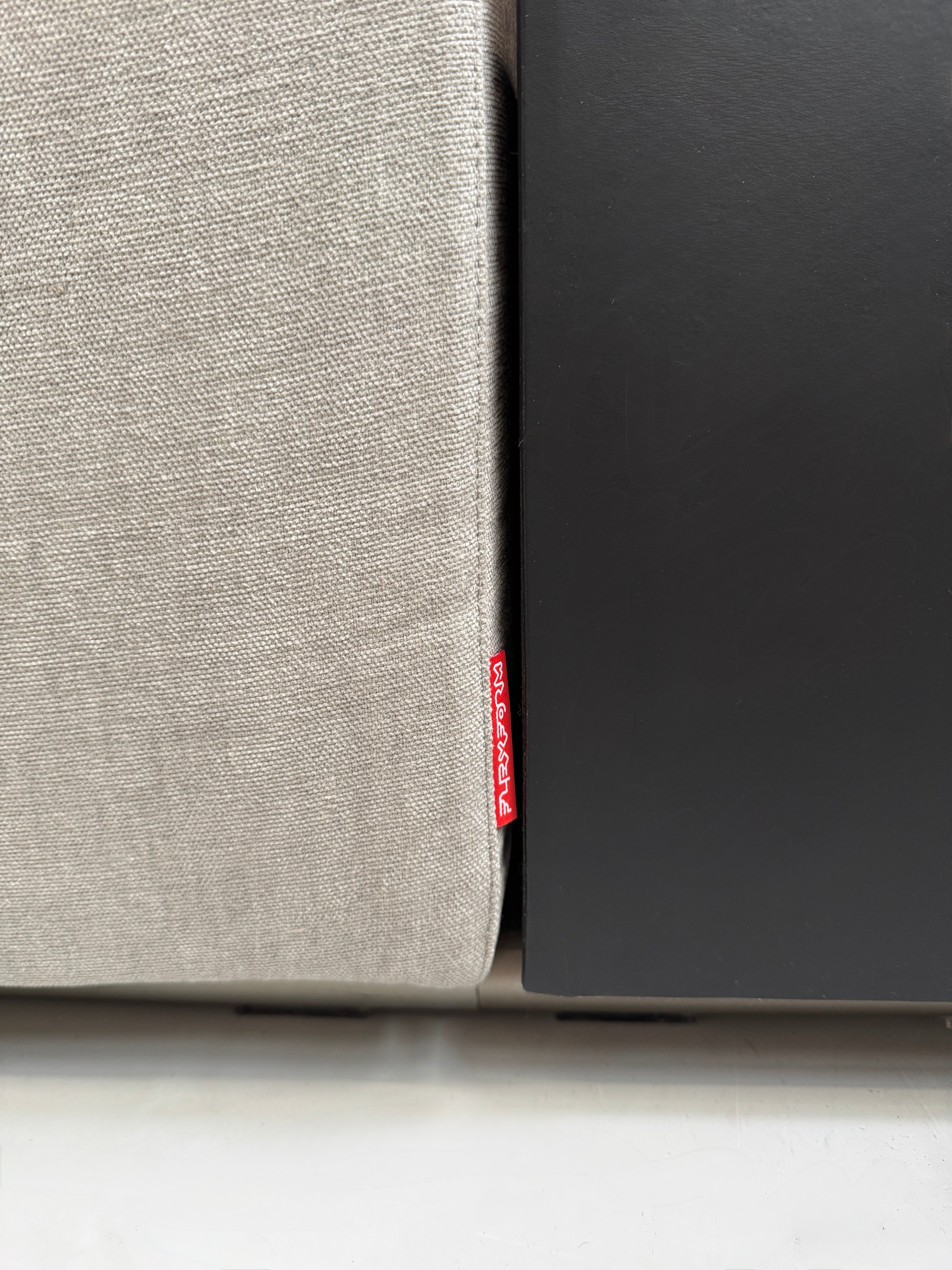 Gebrauchtes graues Flexform Groundpiece Designer Stoff Sofa vor einer Wand, stilvoll und modern eingerichtet.