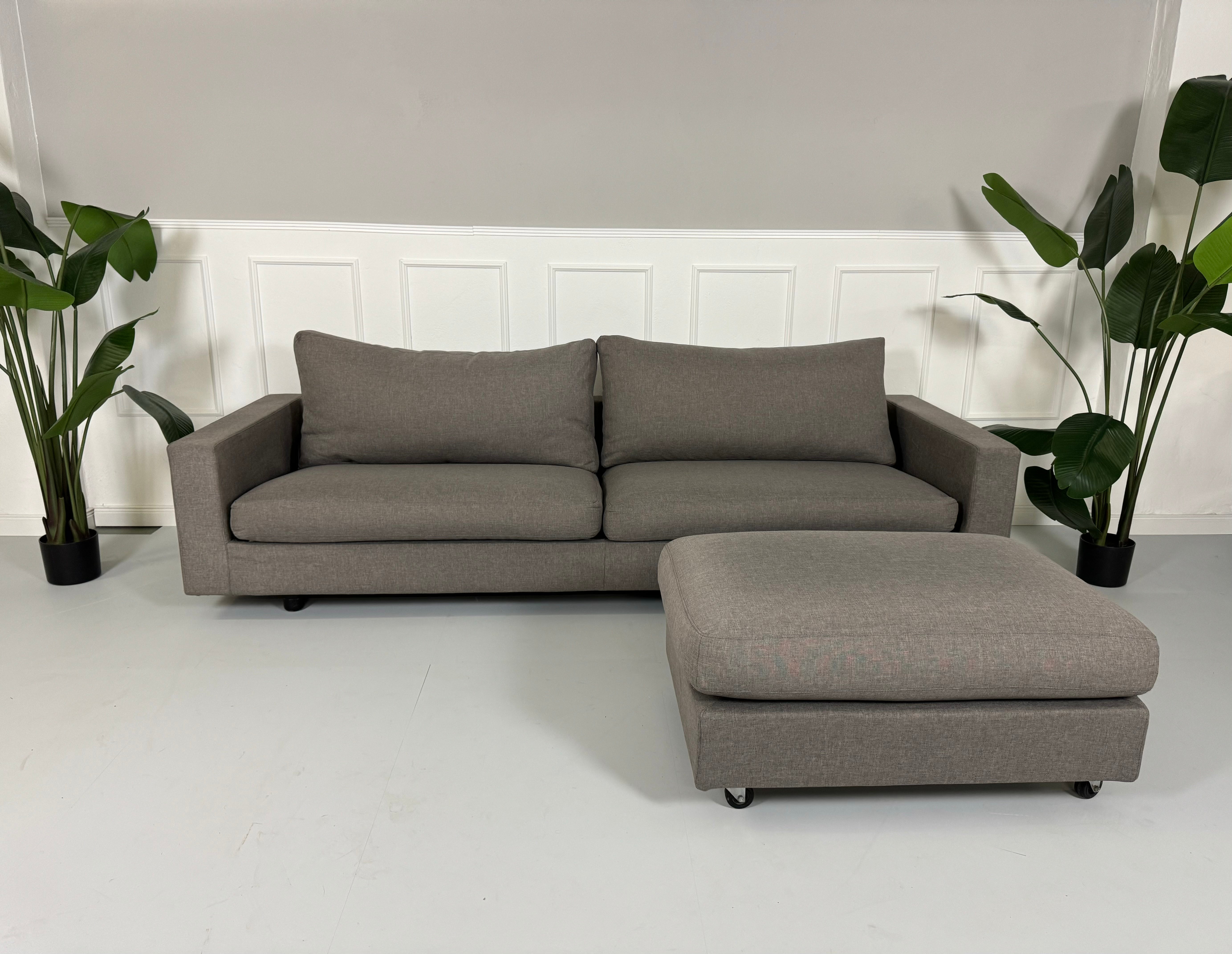 Gebrauchtes Flexform Magnum Stoff Sofa in der Farbe Taupe mit einem Hocker vor einer Wand, stilvoll und modern eingerichtet.
