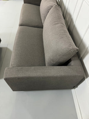 Gebrauchtes Flexform Magnum Stoff Sofa in der Farbe Taupe mit einem Hocker vor einer Wand, stilvoll und modern eingerichtet.