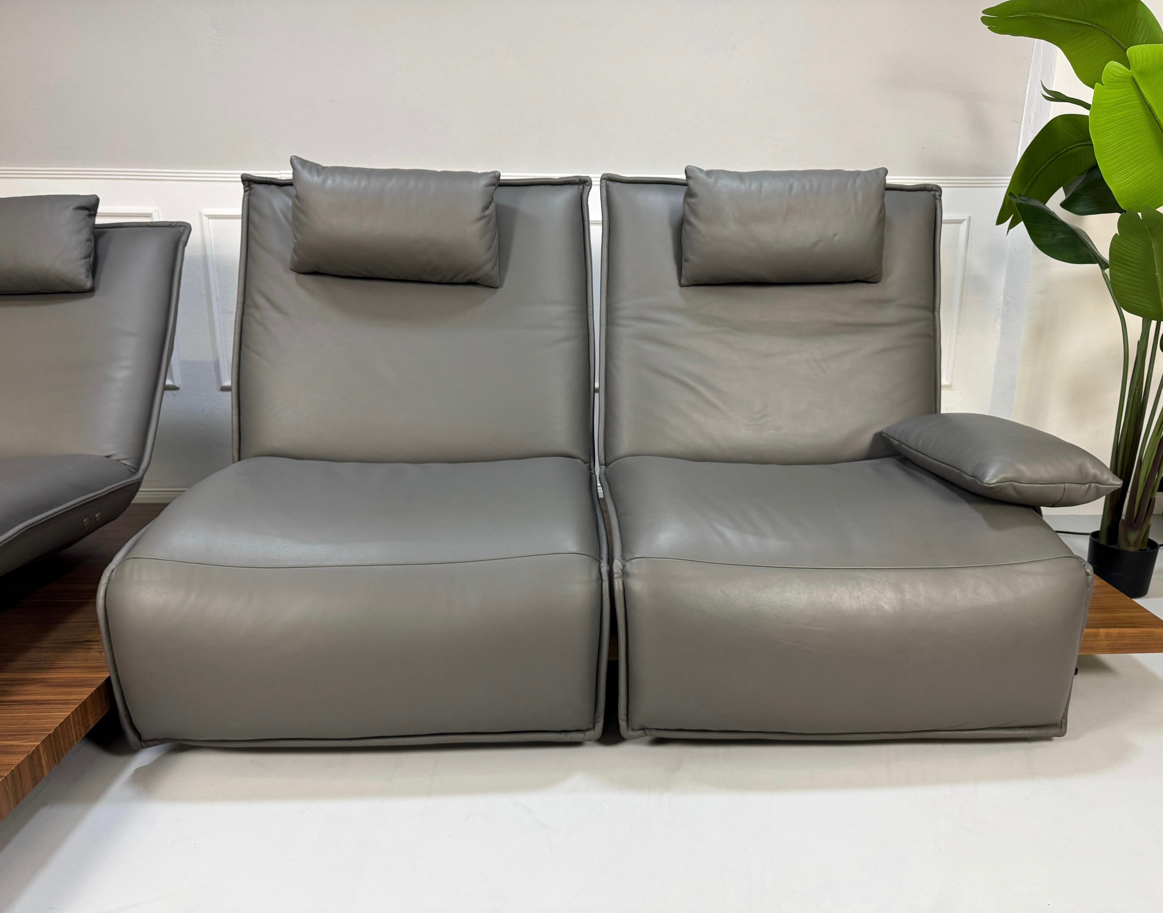 Gebrauchtes graues Koinor Epos Designer Leder Sofa vor einer Wand, stilvoll und modern eingerichtet.