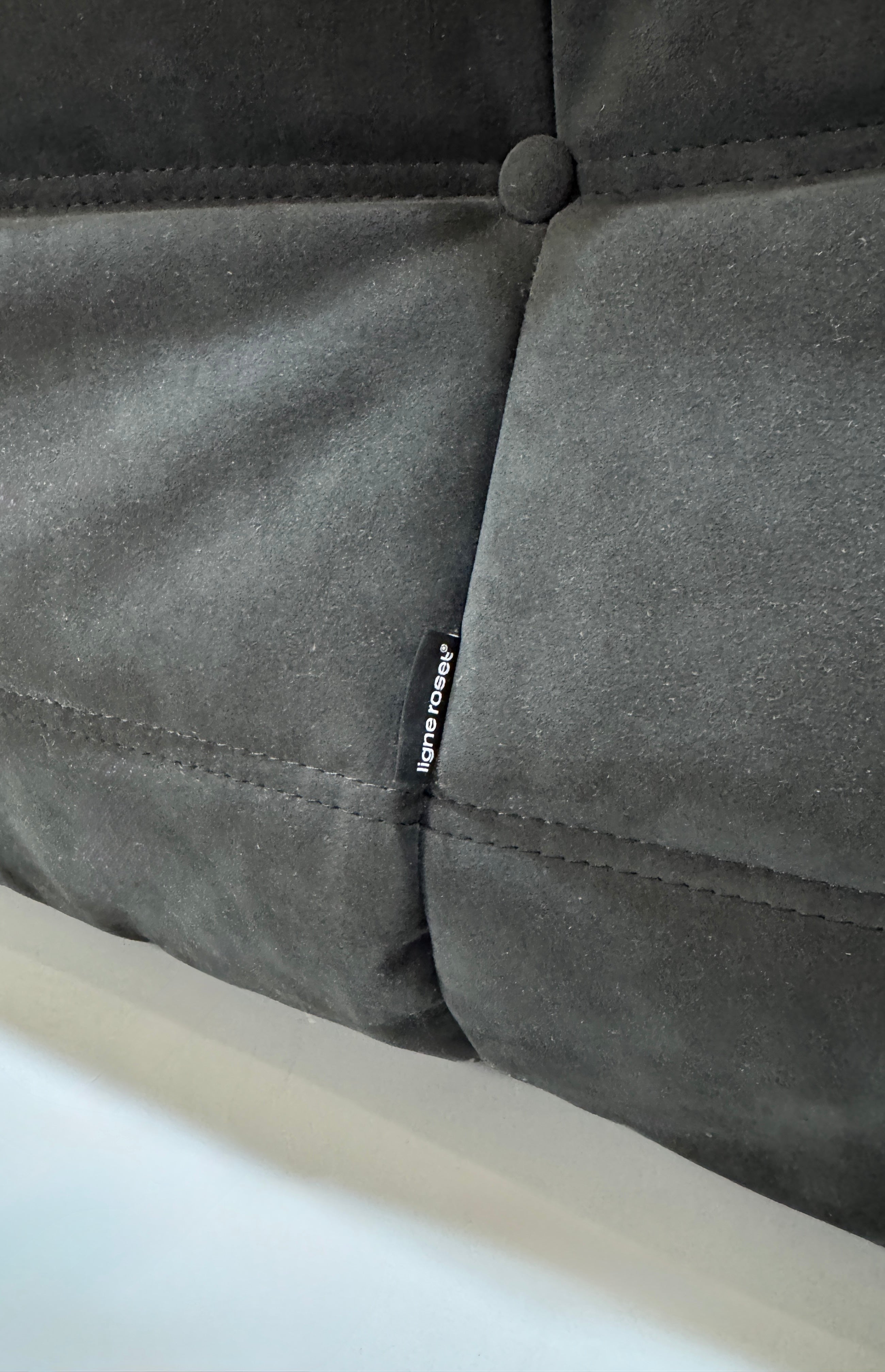 Gebrauchtes graues Ligne Roset Togo Designer Stoff Sofa vor einer Wand, stilvoll und modern eingerichtet.
