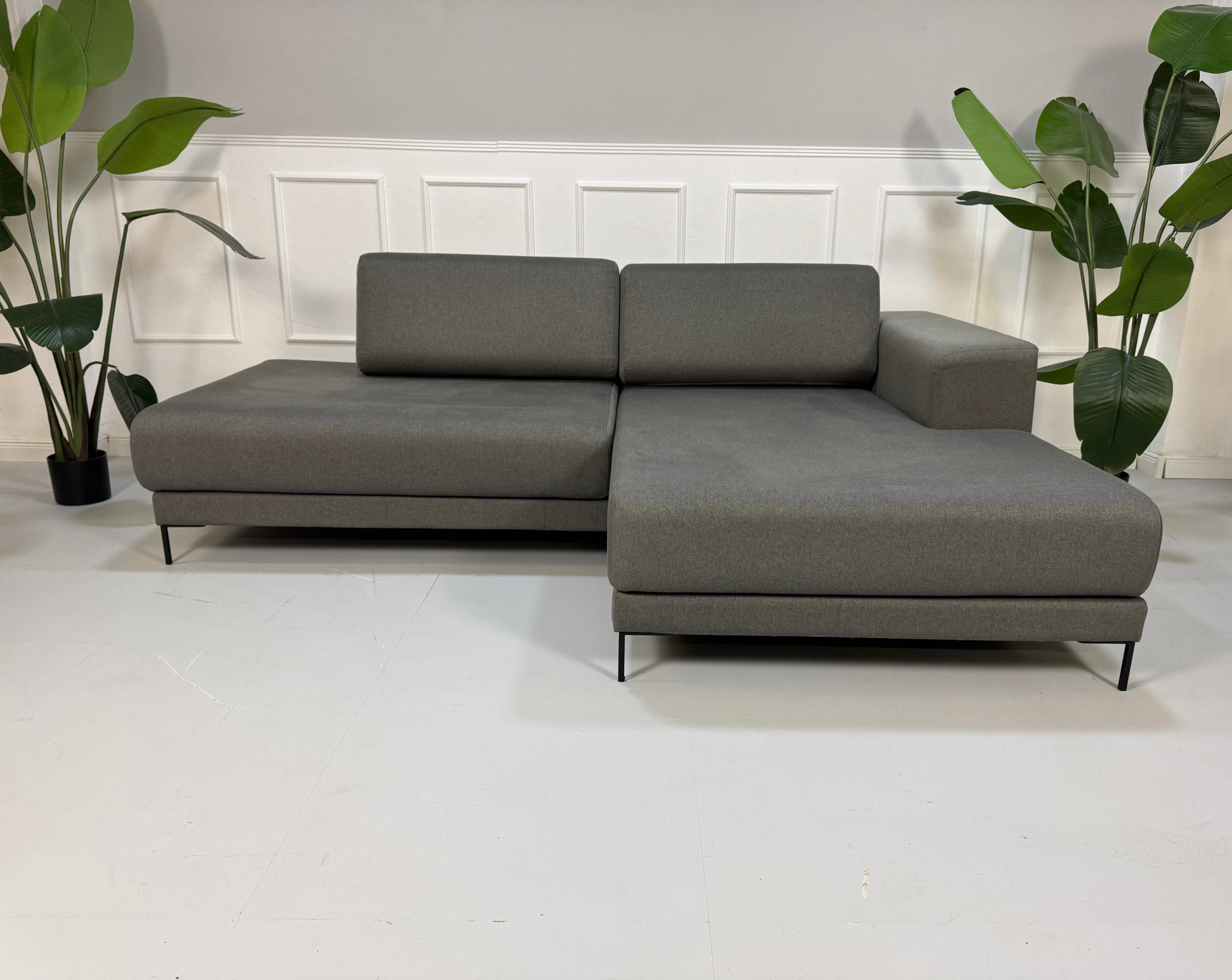 Gebrauchtes graues MYCS Tyme Designer Stoff Sofa vor einer Wand, stilvoll und modern eingerichtet.