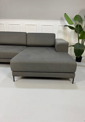 Gebrauchtes graues MYCS Tyme Designer Stoff Sofa vor einer Wand, stilvoll und modern eingerichtet.