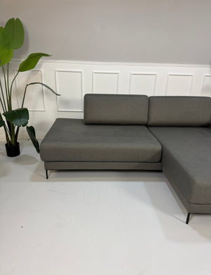 Gebrauchtes graues MYCS Tyme Designer Stoff Sofa vor einer Wand, stilvoll und modern eingerichtet.