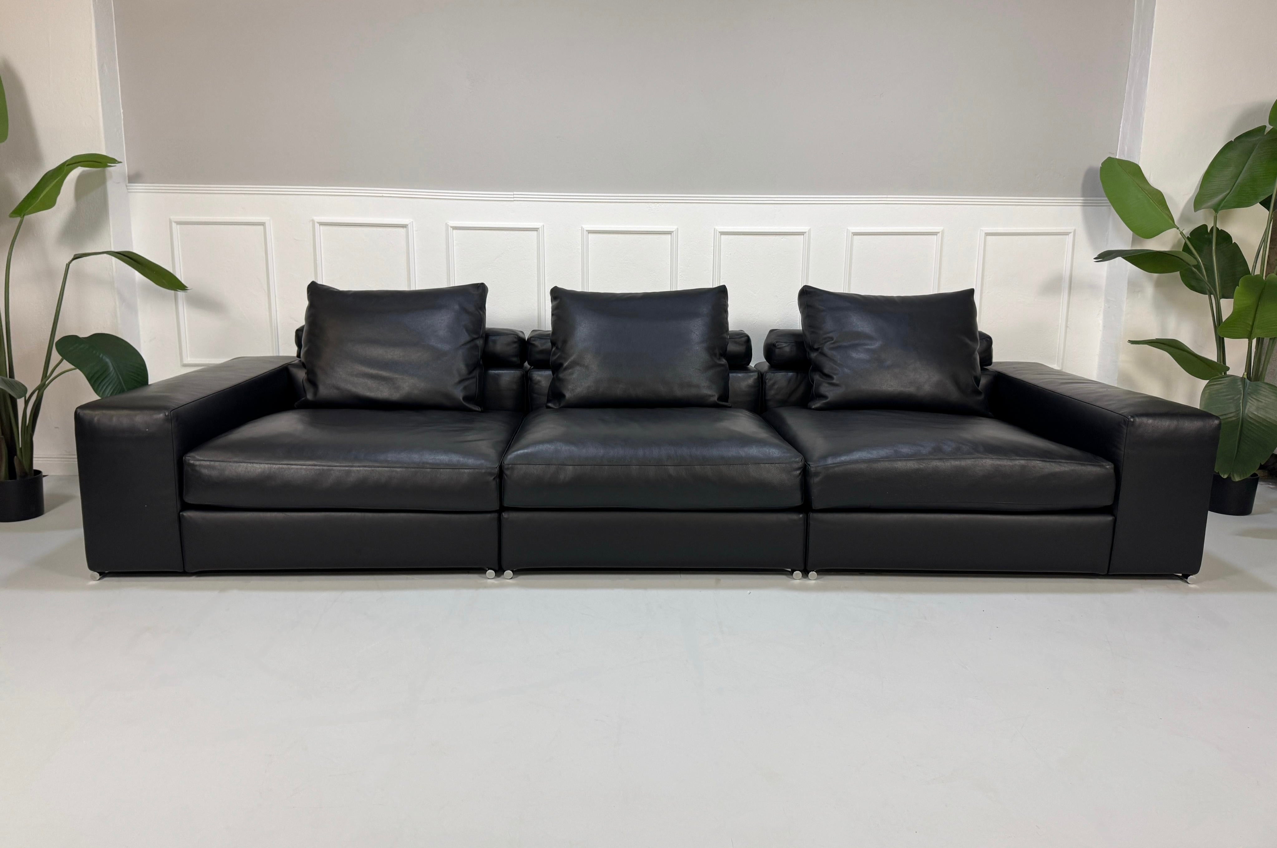 Gebrauchtes schwarzes Minotti Designer Leder Sofa vor einer Wand, stilvoll und modern eingerichtet.