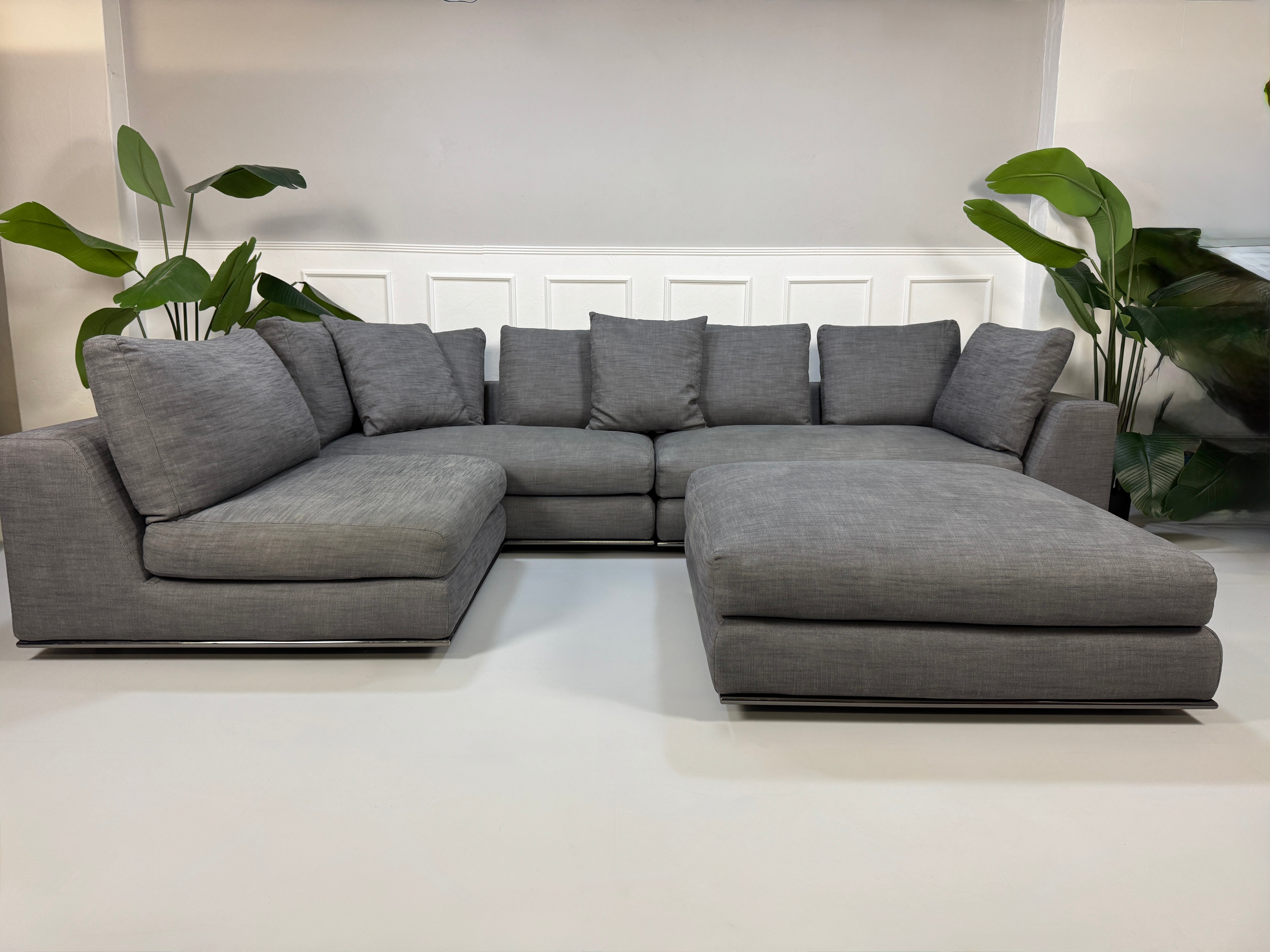 Gebrauchtes graues Minotti Hamilton Designer Stoff Sofa mit einem Hocker vor einer Wand, stilvoll und modern eingerichtet.