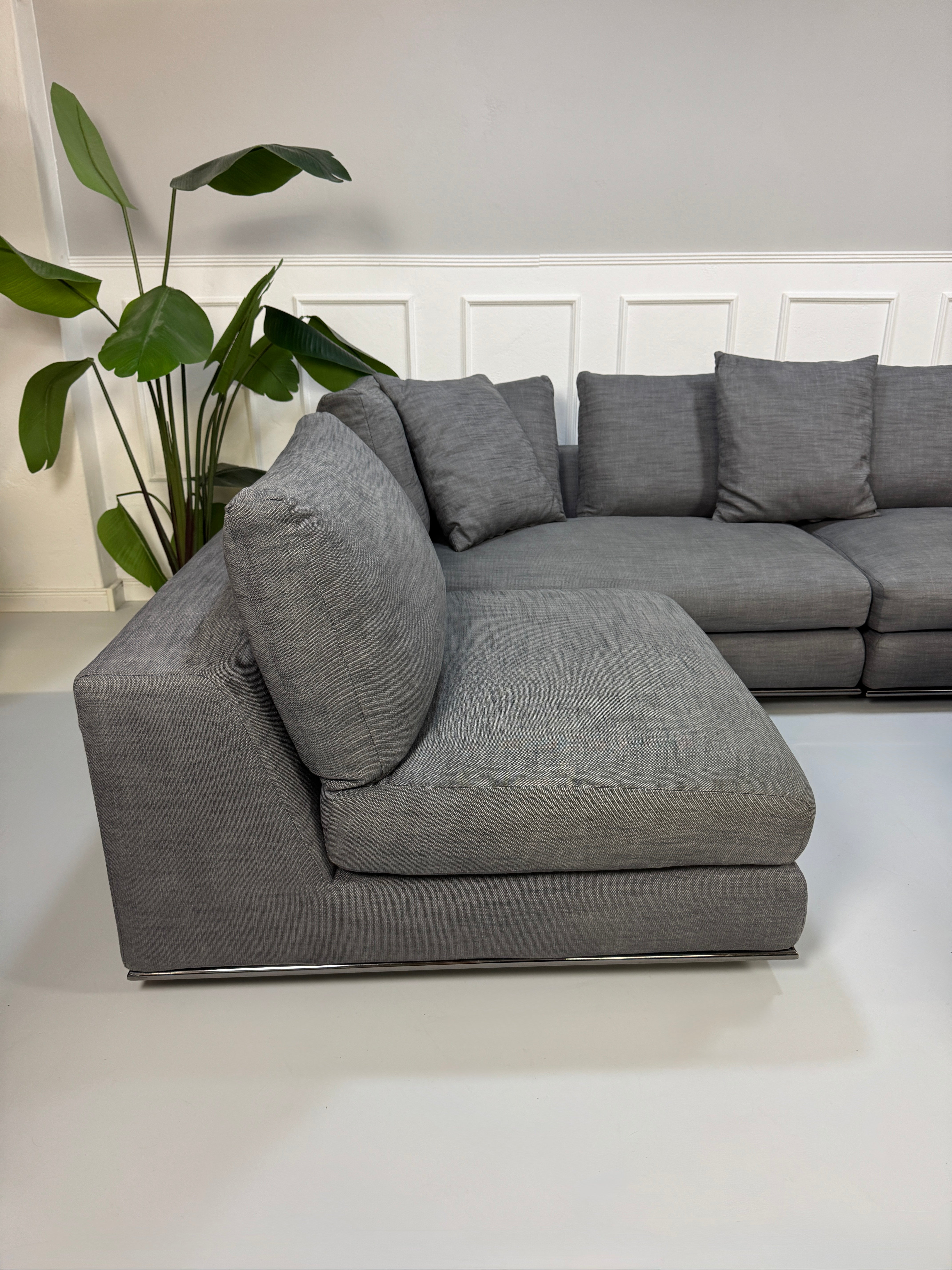 Gebrauchtes graues Minotti Hamilton Designer Stoff Sofa mit einem Hocker vor einer Wand, stilvoll und modern eingerichtet.