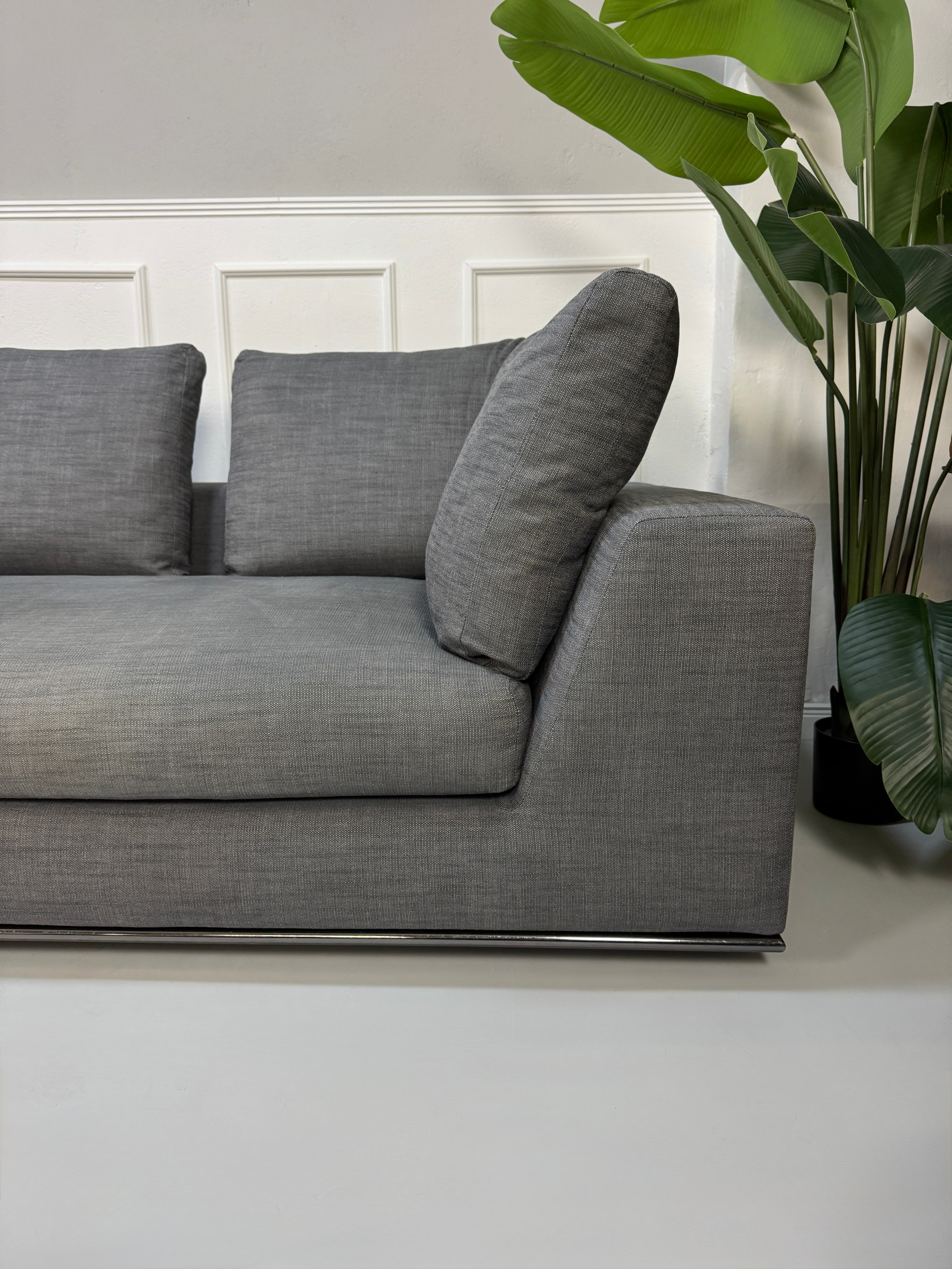 Gebrauchtes graues Minotti Hamilton Designer Stoff Sofa mit einem Hocker vor einer Wand, stilvoll und modern eingerichtet.