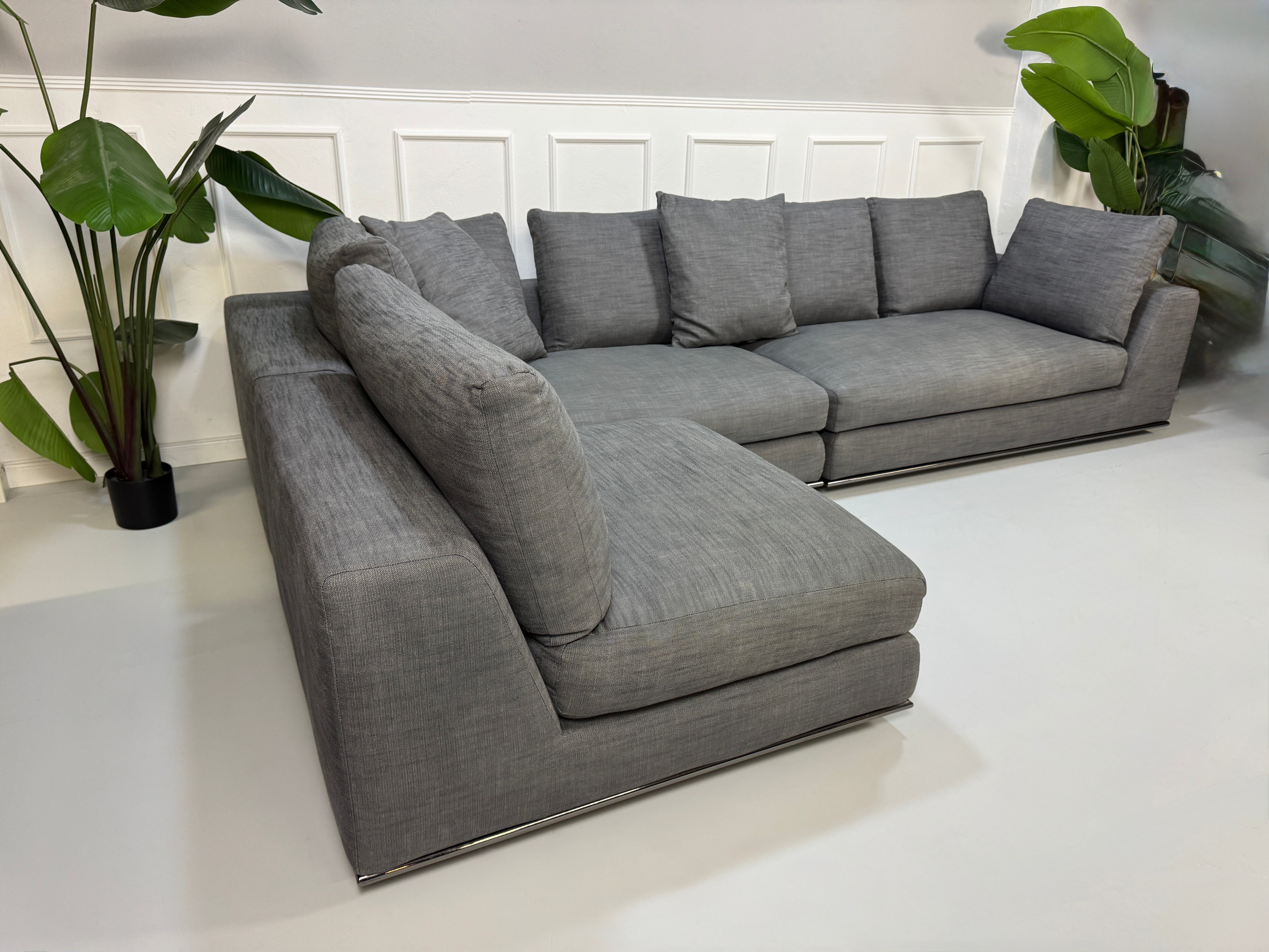 Gebrauchtes graues Minotti Hamilton Designer Stoff Sofa mit einem Hocker vor einer Wand, stilvoll und modern eingerichtet.