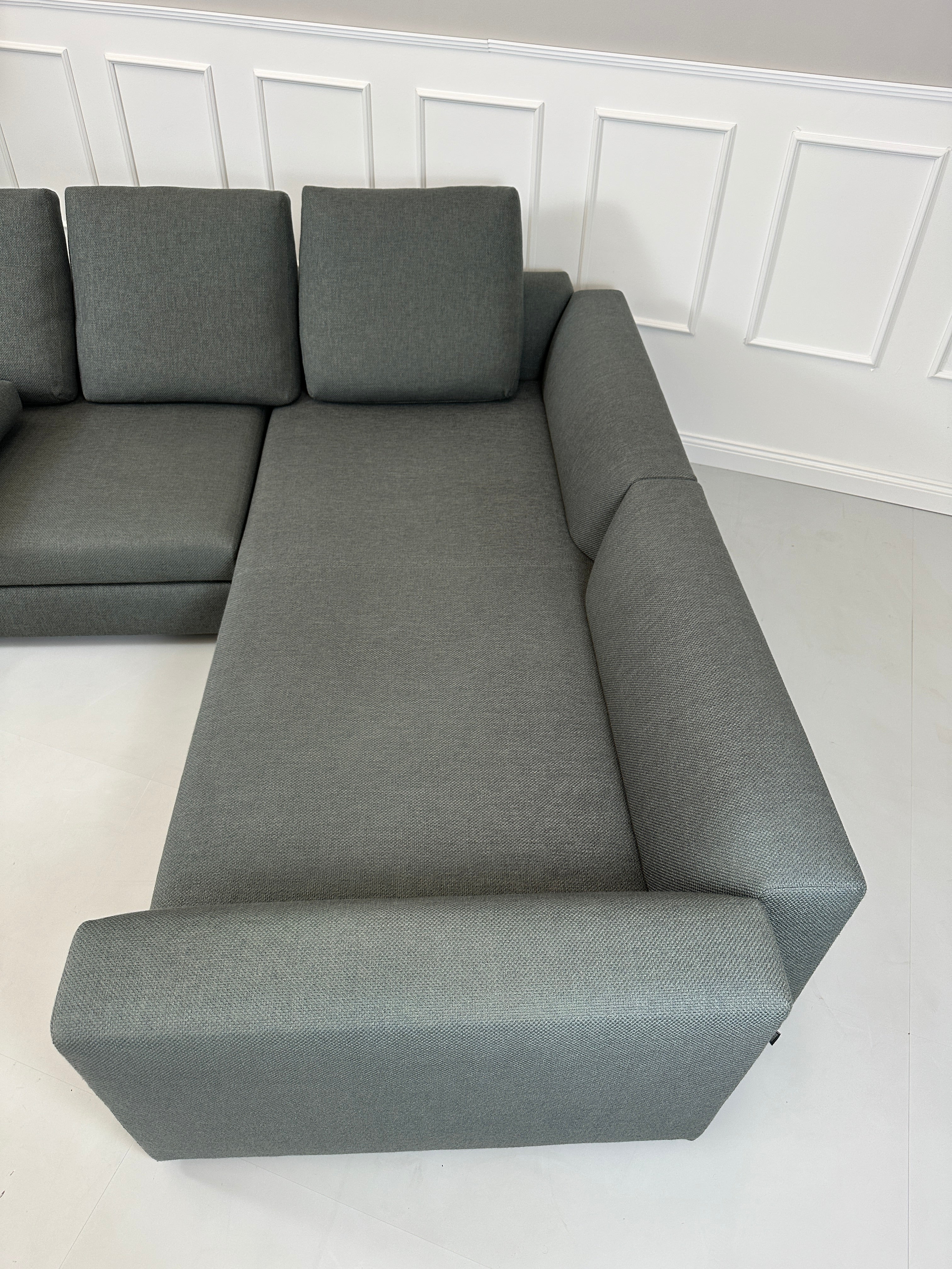 Gebrauchtes grünes Minotti Kline Designer Stoff Sofa vor einer Wand, stilvoll und modern eingerichtet mit Tisch.