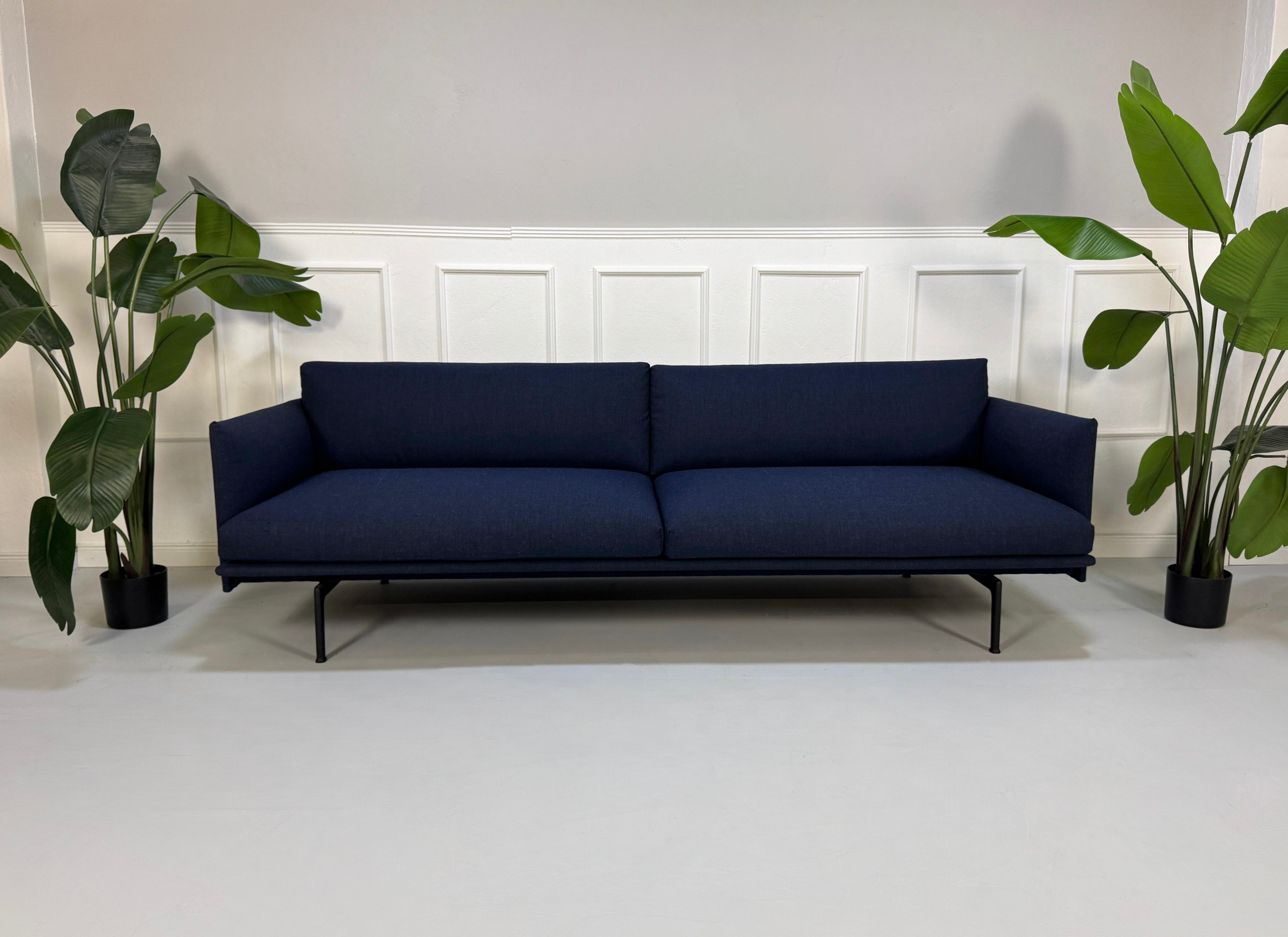 Gebrauchtes blaues Muuto Outline Designer Stoff Sofa vor einer Wand, stilvoll und modern eingerichtet.