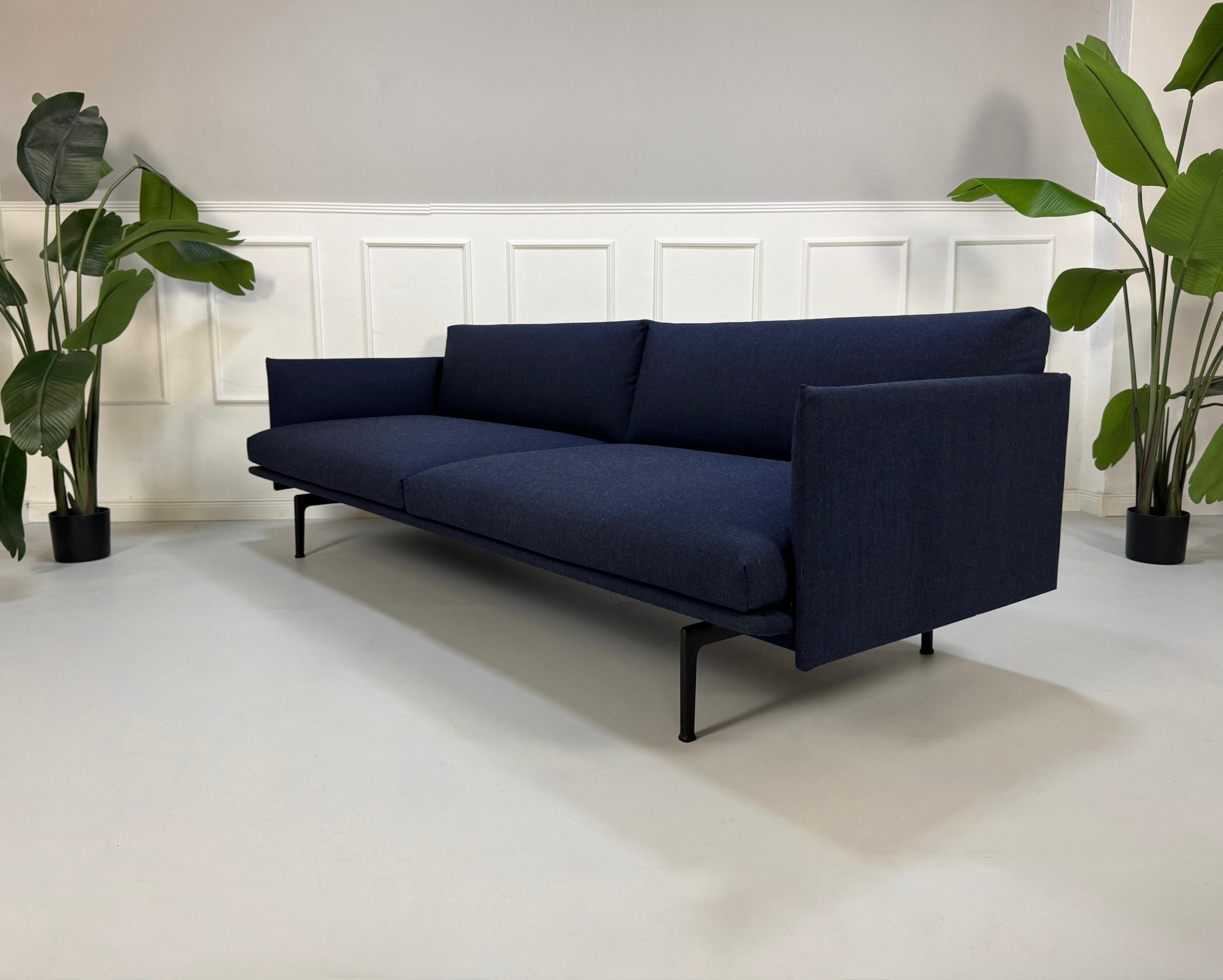 Gebrauchtes blaues Muuto Outline Designer Stoff Sofa vor einer Wand, stilvoll und modern eingerichtet.