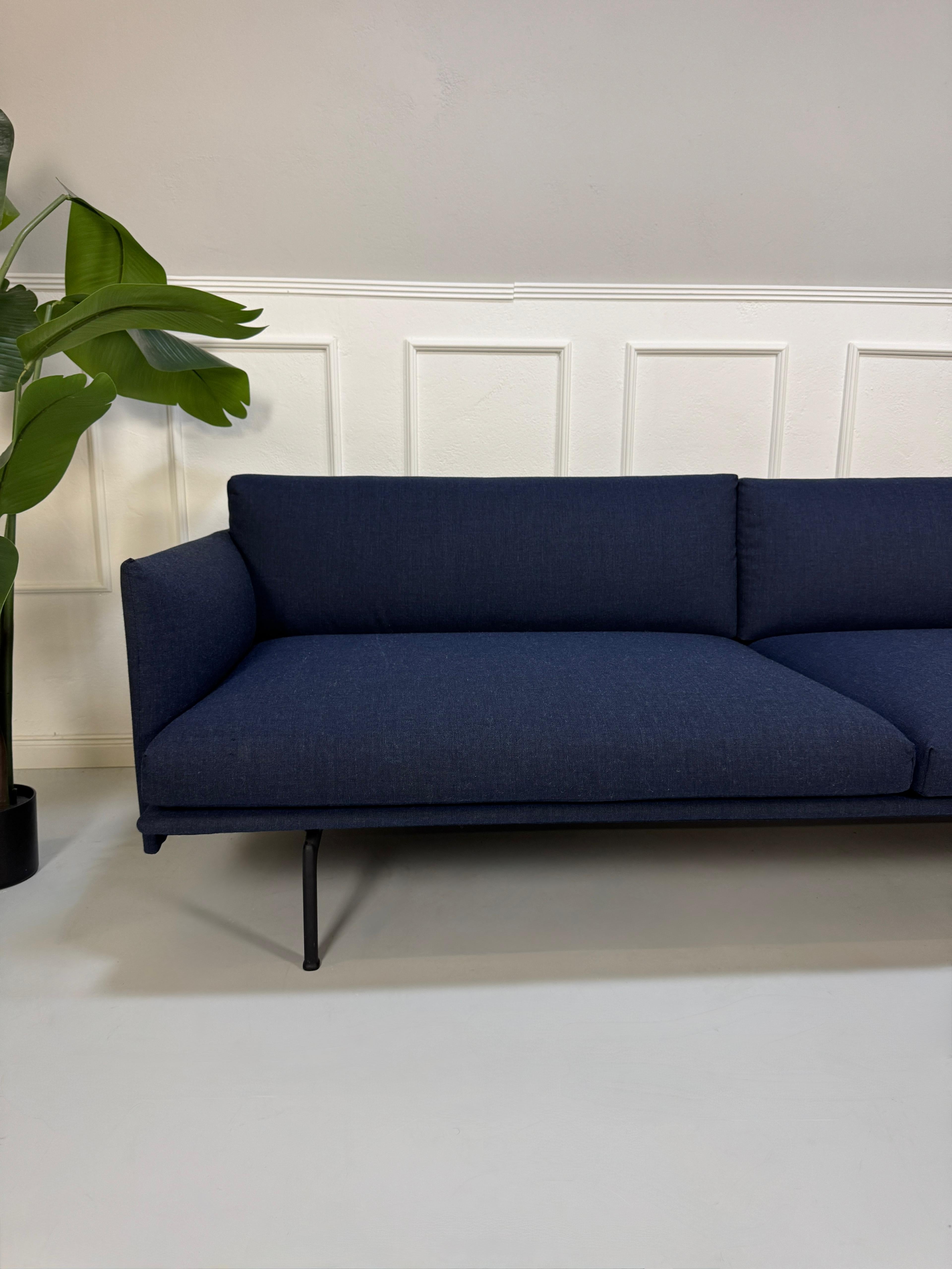 Gebrauchtes blaues Muuto Outline Designer Stoff Sofa vor einer Wand, stilvoll und modern eingerichtet.