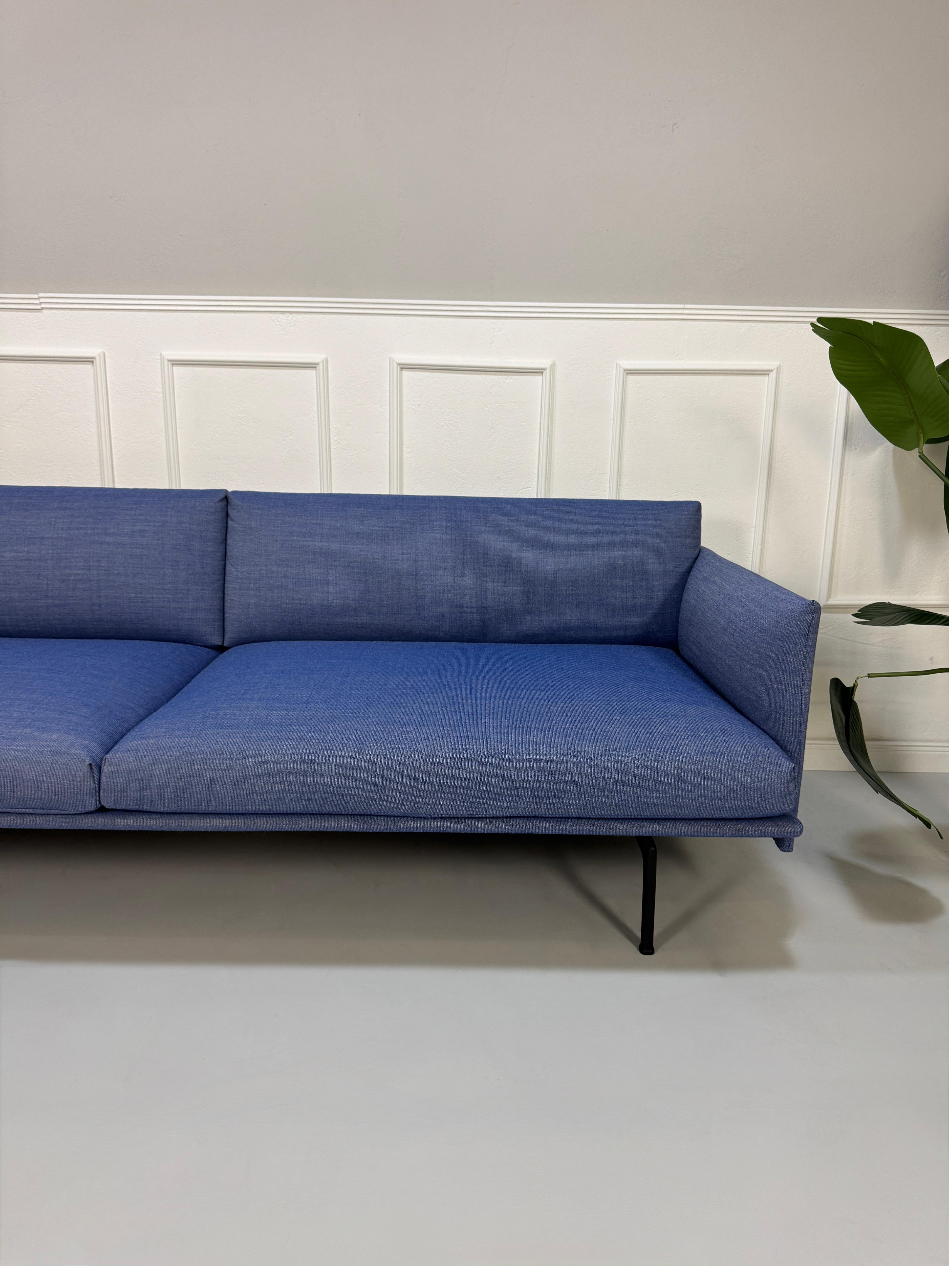 Gebrauchtes blaues Muuto Outline Designer Stoff Sofa vor einer Wand, stilvoll und modern eingerichtet.