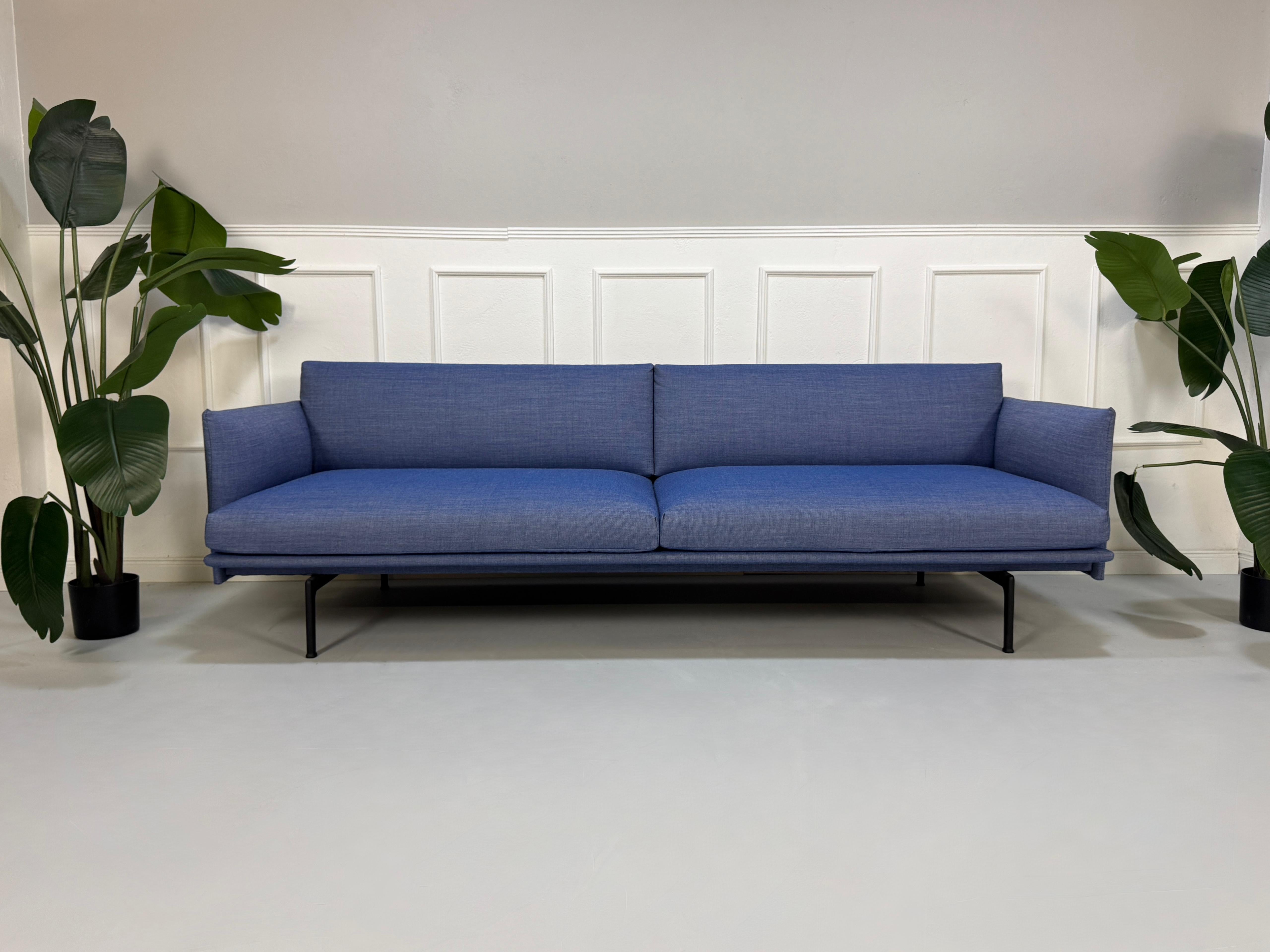 Gebrauchtes blaues Muuto Outline Designer Stoff Sofa vor einer Wand, stilvoll und modern eingerichtet.