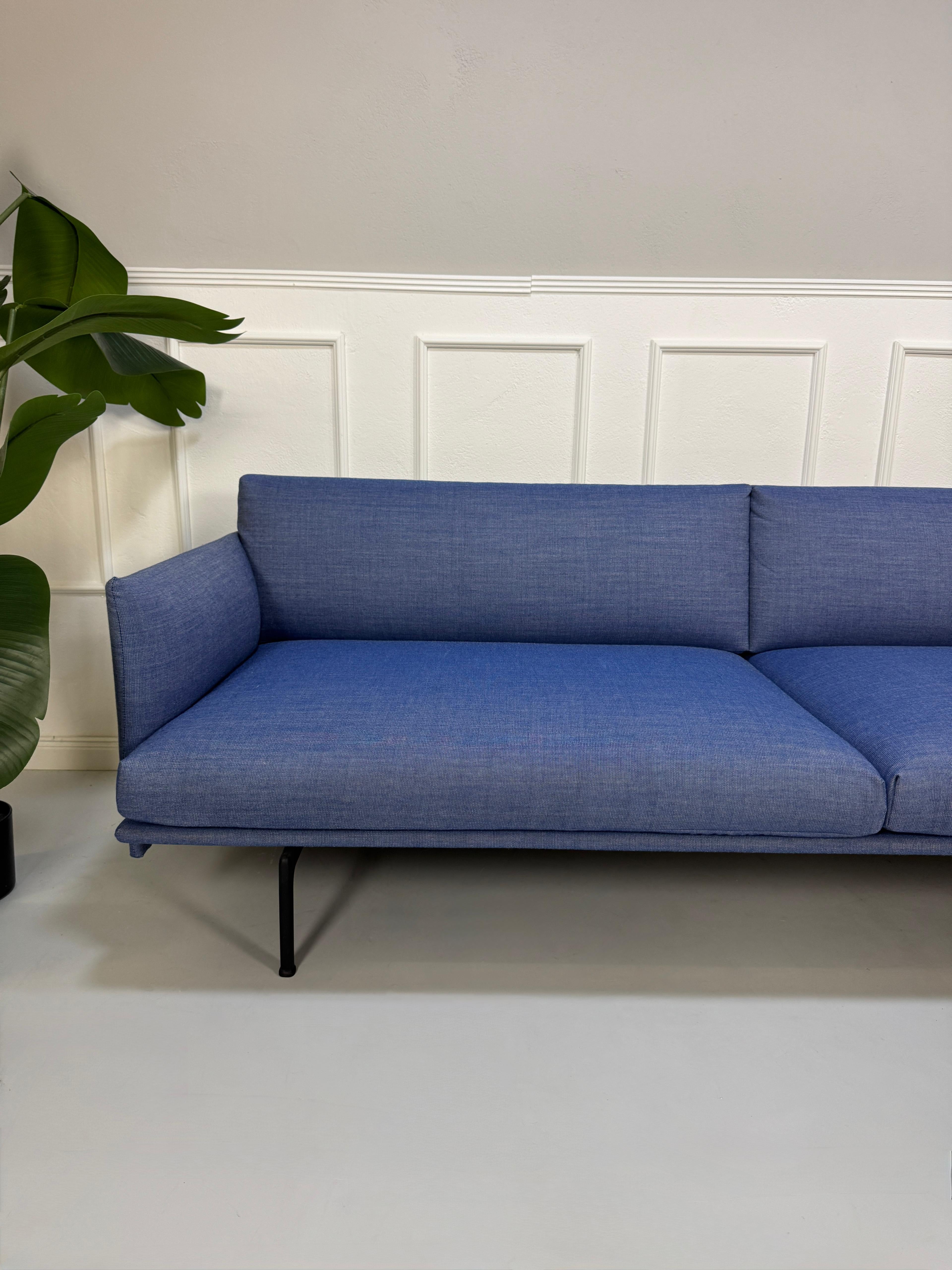 Gebrauchtes blaues Muuto Outline Designer Stoff Sofa vor einer Wand, stilvoll und modern eingerichtet.