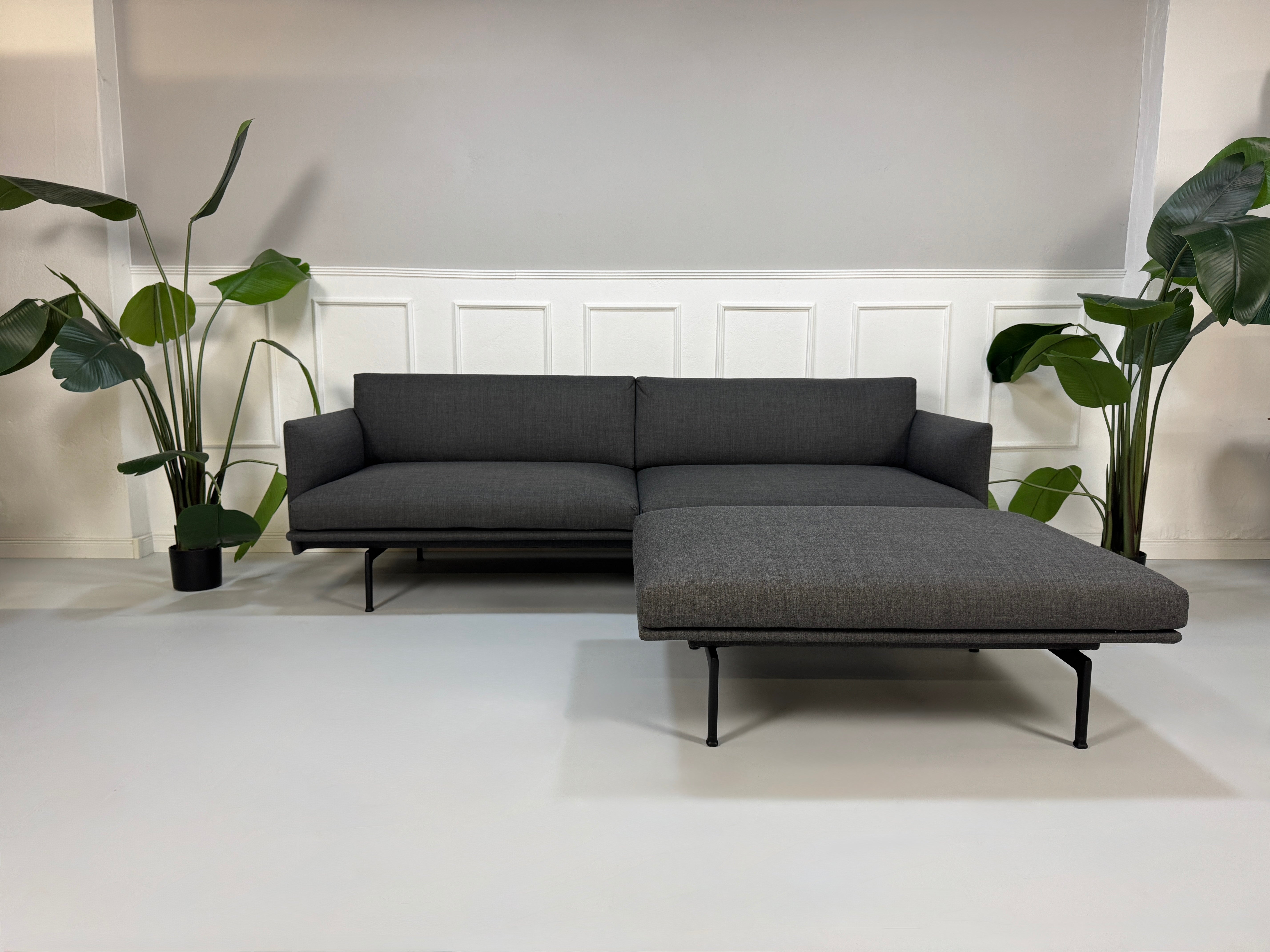 Gebrauchtes graues Muuto Outline Designer Stoff Sofa mit einem Hocker vor einer Wand, stilvoll und modern eingerichtet.