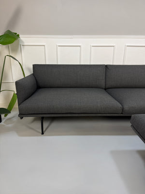 Gebrauchtes graues Muuto Outline Designer Stoff Sofa mit einem Hocker vor einer Wand, stilvoll und modern eingerichtet.