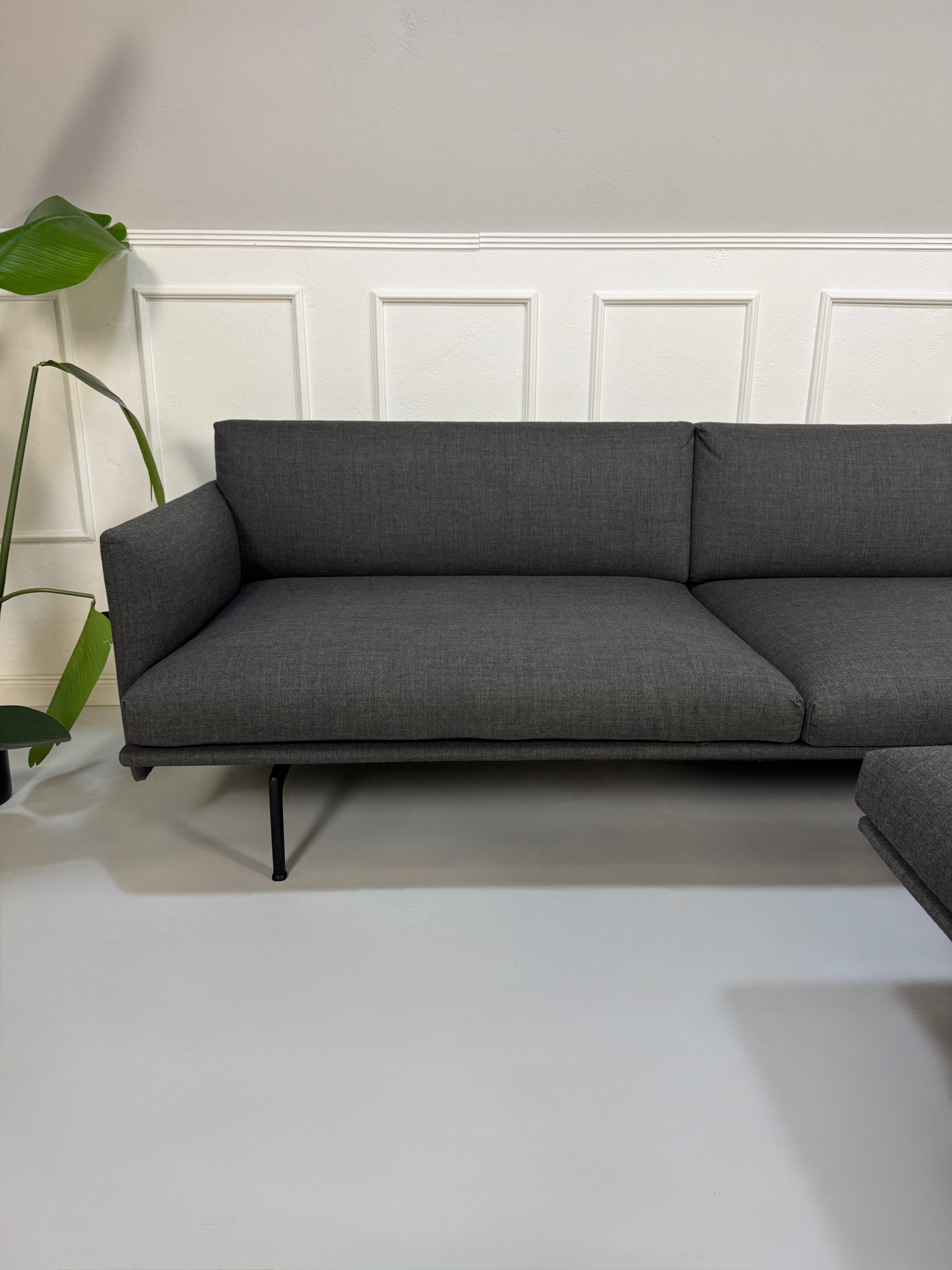 Gebrauchtes graues Muuto Outline Designer Stoff Sofa mit einem Hocker vor einer Wand, stilvoll und modern eingerichtet.