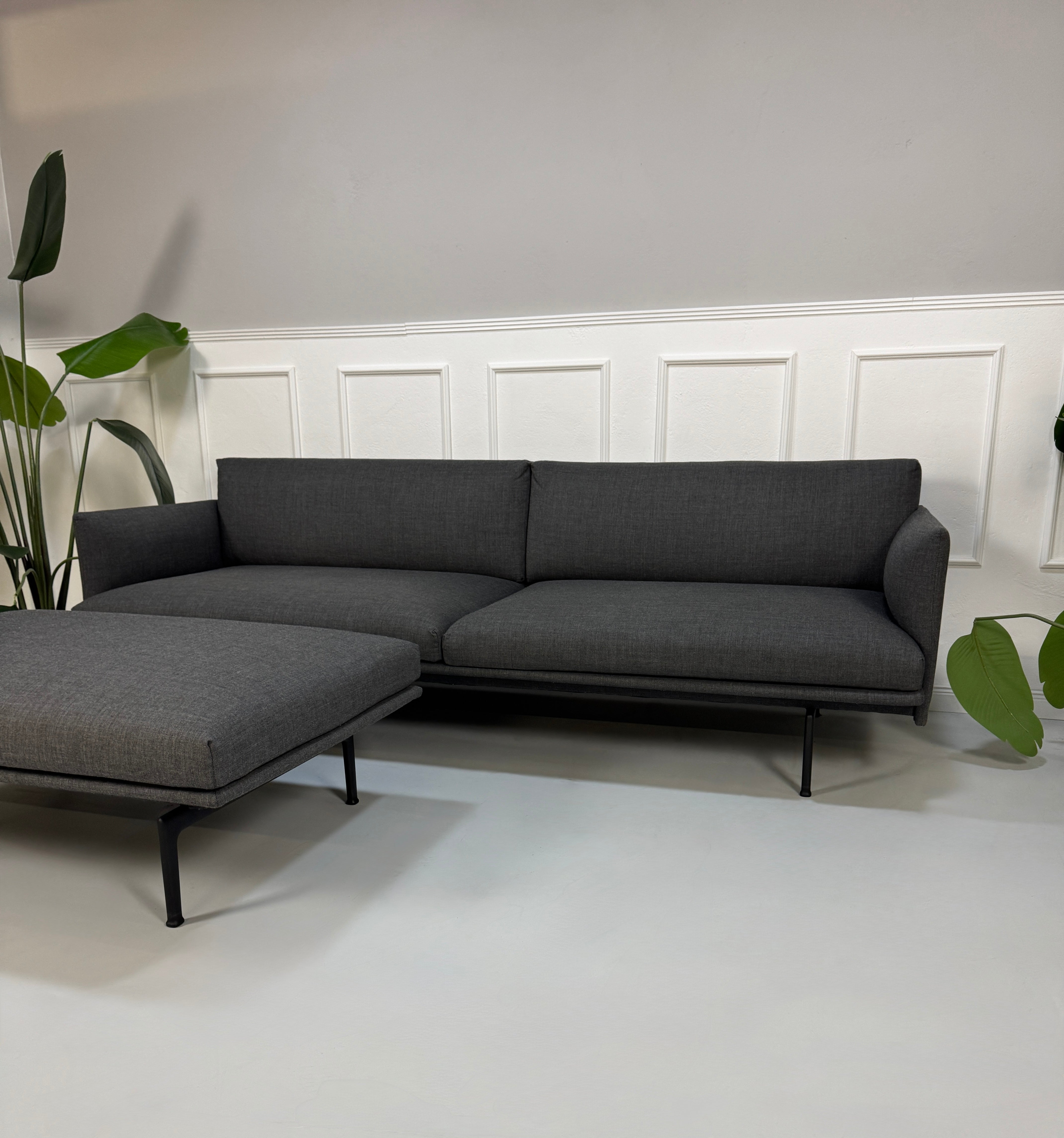 Gebrauchtes graues Muuto Outline Designer Stoff Sofa mit einem Hocker vor einer Wand, stilvoll und modern eingerichtet.