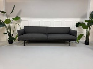 Gebrauchtes graues Muuto Outline Designer Stoff Sofa mit einem Hocker vor einer Wand, stilvoll und modern eingerichtet.