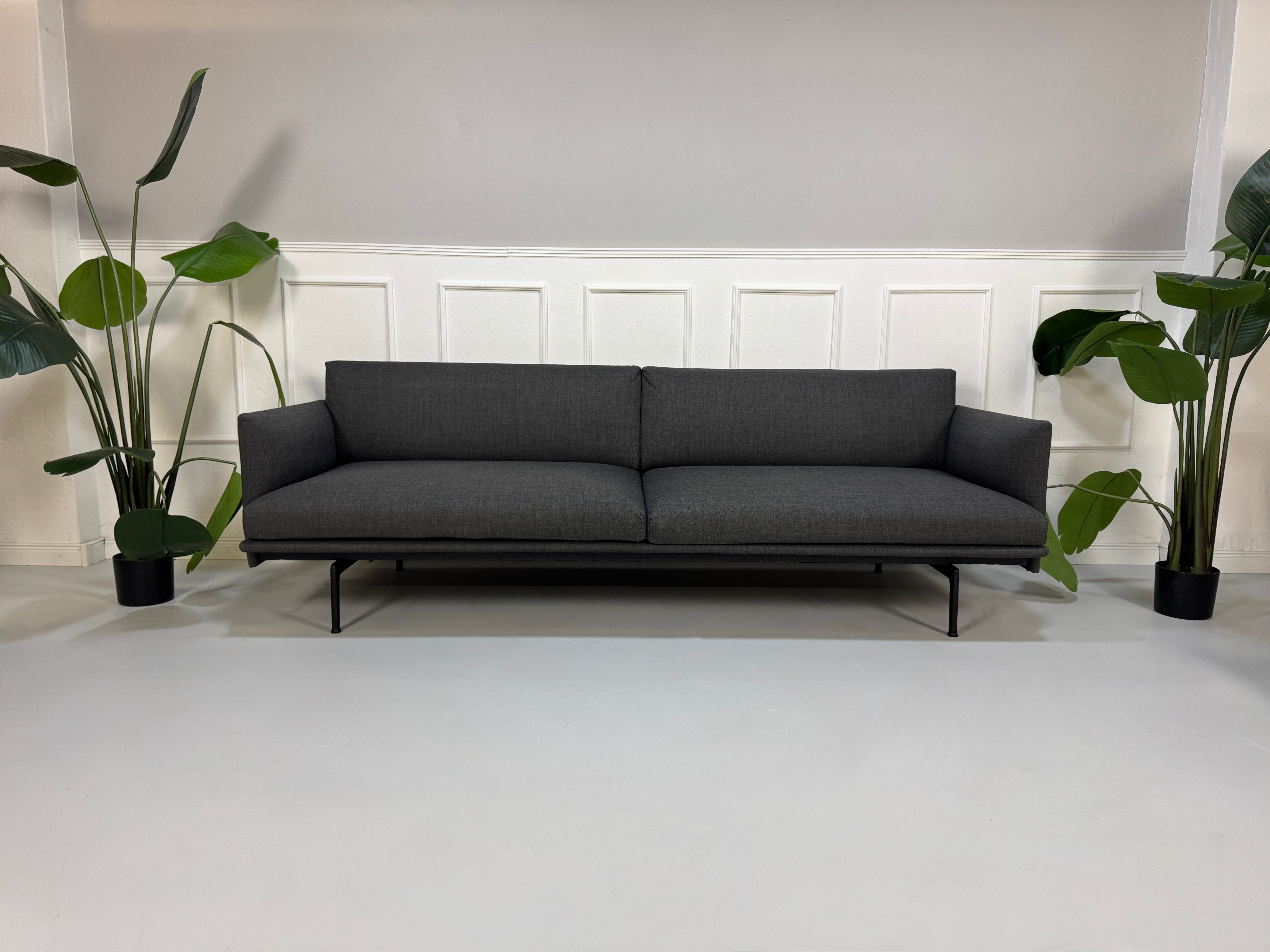 Gebrauchtes graues Muuto Outline Designer Stoff Sofa mit einem Hocker vor einer Wand, stilvoll und modern eingerichtet.