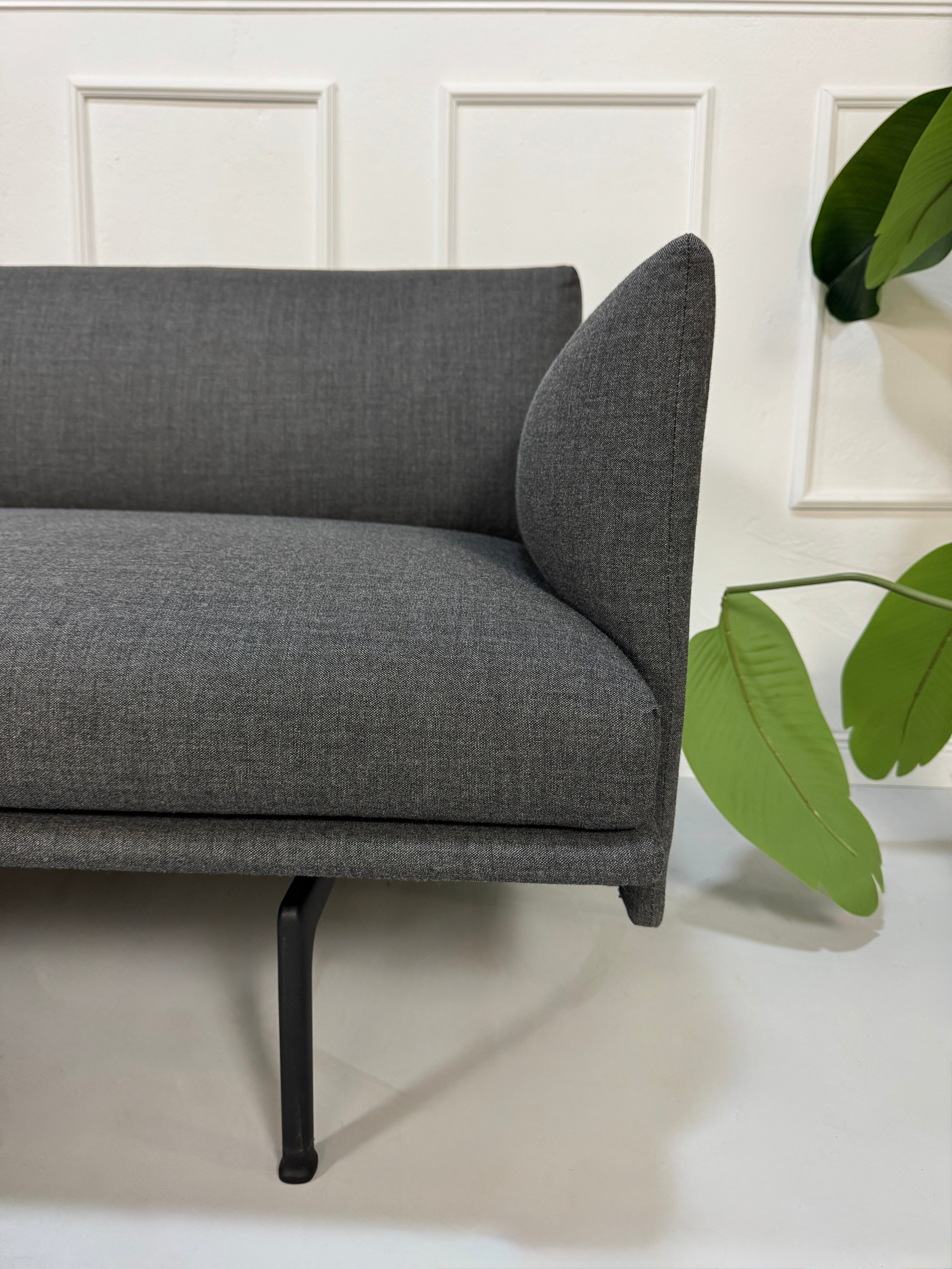 Gebrauchtes graues Muuto Outline Designer Stoff Sofa mit einem Hocker vor einer Wand, stilvoll und modern eingerichtet.
