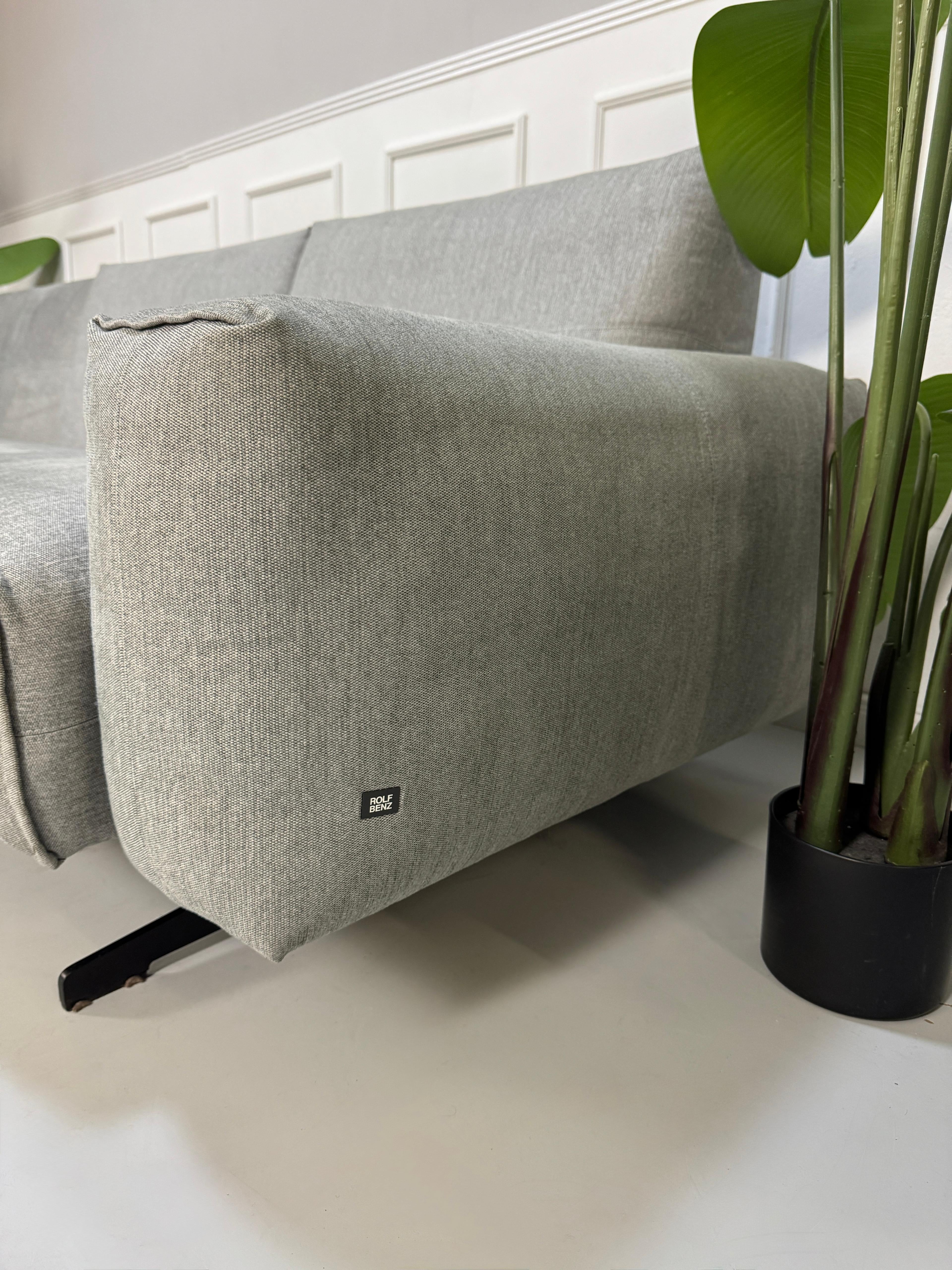 Gebrauchtes graues Rolf Benz 50 Designer Stoff Sofa vor einer Wand, stilvoll und modern eingerichtet.