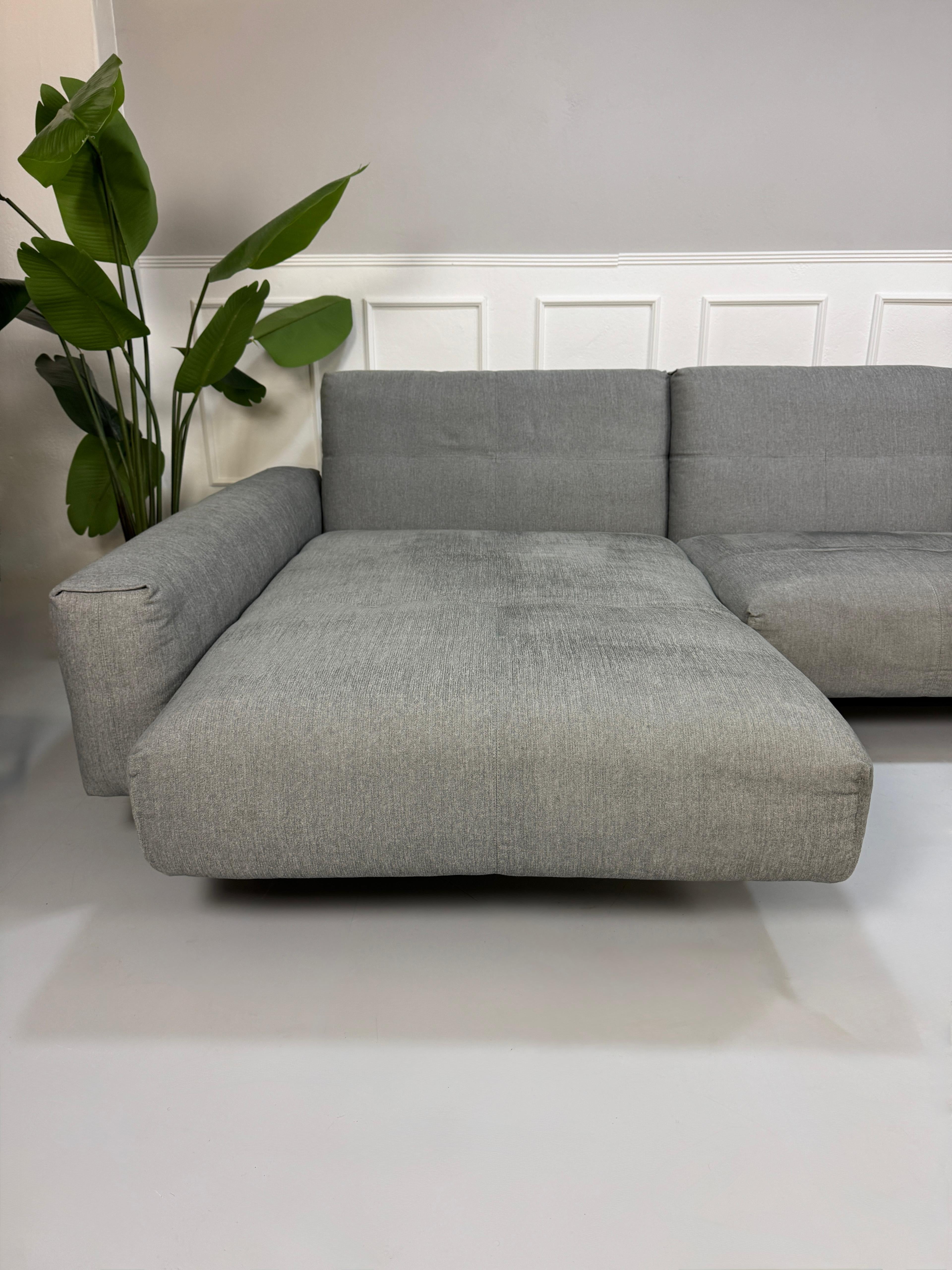 Gebrauchtes graues Rolf Benz 50 Designer Stoff Sofa vor einer Wand, stilvoll und modern eingerichtet.