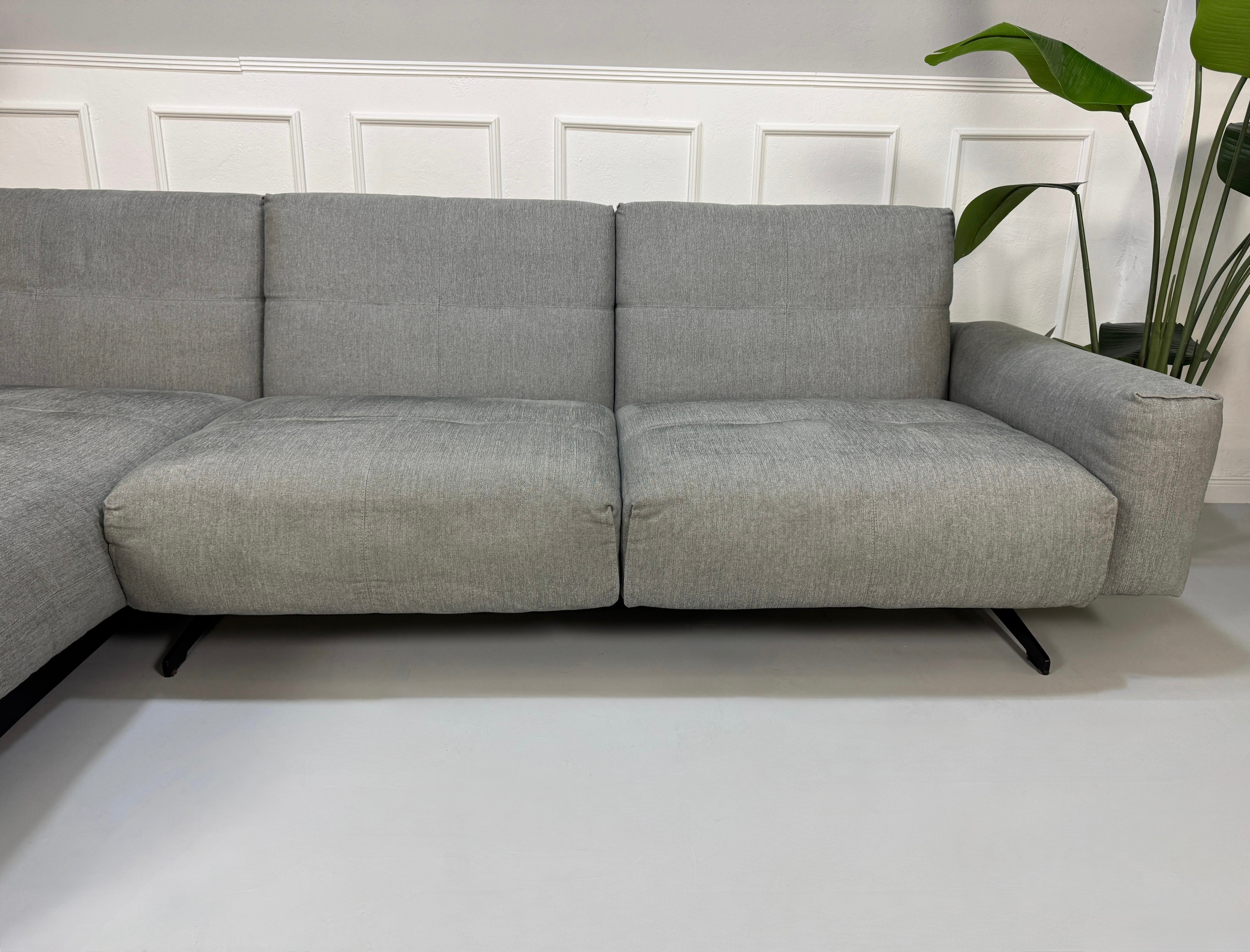 Gebrauchtes graues Rolf Benz 50 Designer Stoff Sofa vor einer Wand, stilvoll und modern eingerichtet.