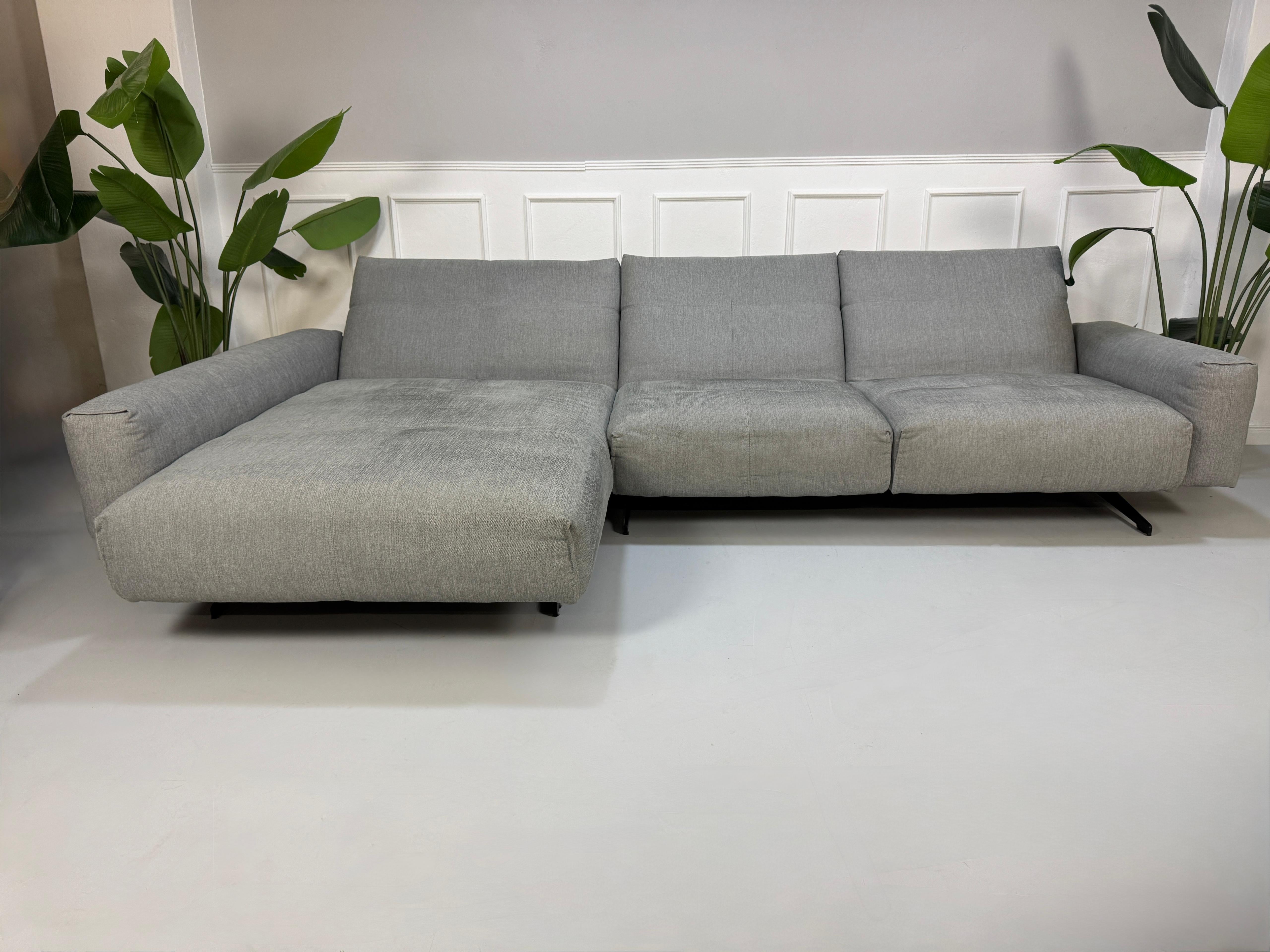 Gebrauchtes graues Rolf Benz 50 Designer Stoff Sofa vor einer Wand, stilvoll und modern eingerichtet.