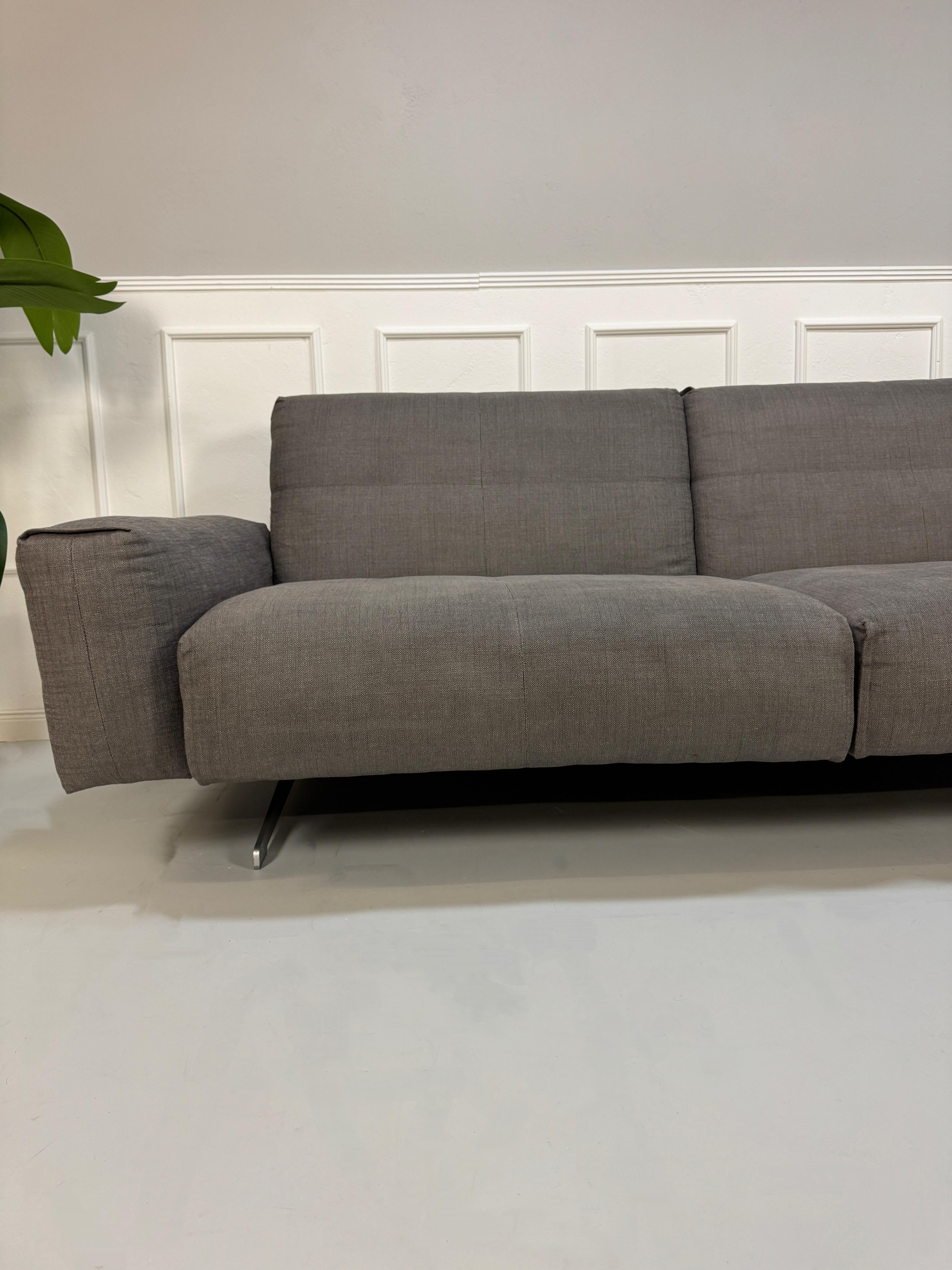 Gebrauchtes graues Rolf Benz 50 Designer Stoff Sofa vor einer Wand, stilvoll und modern eingerichtet.