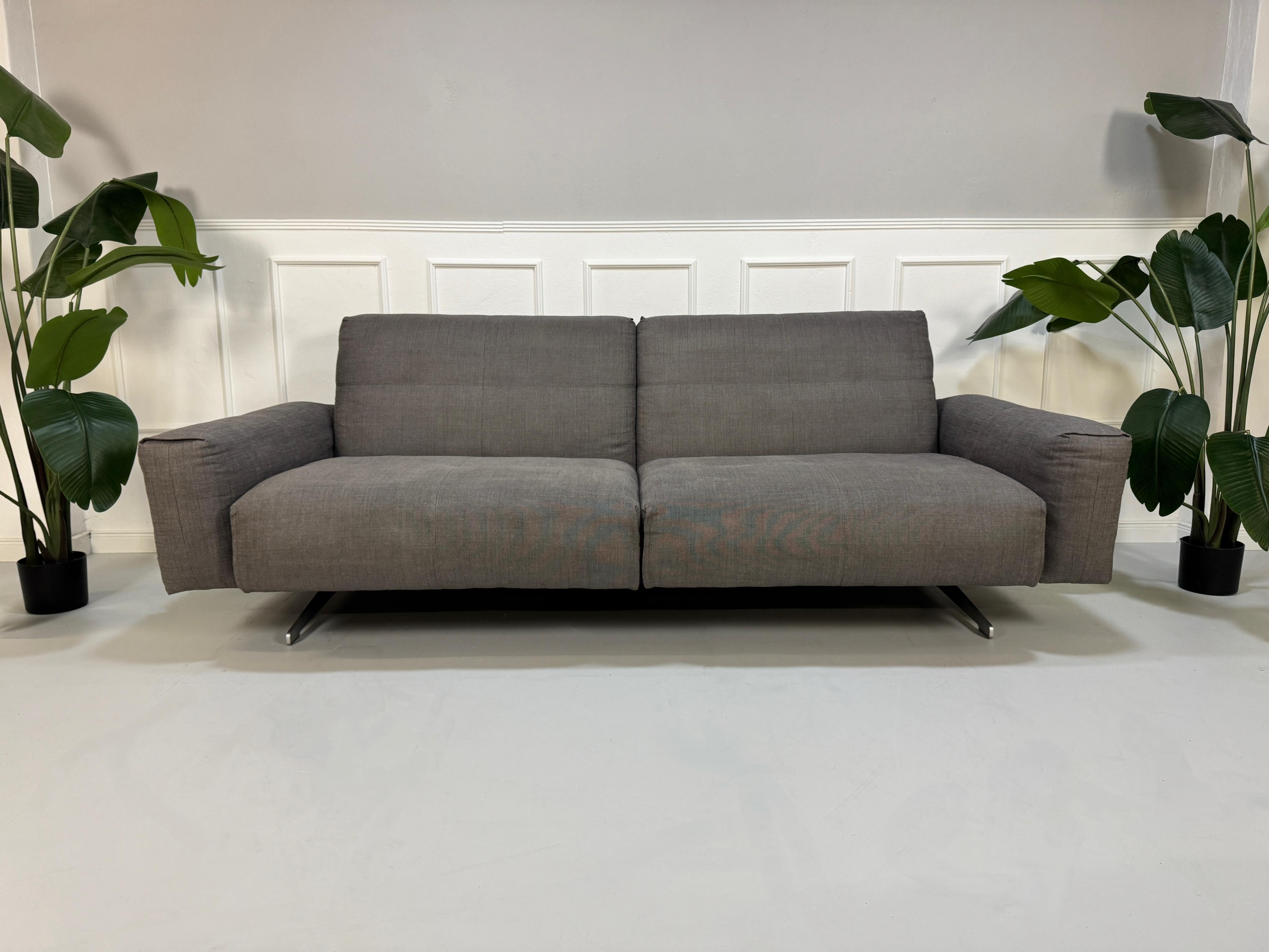 Gebrauchtes graues Rolf Benz 50 Designer Stoff Sofa vor einer Wand, stilvoll und modern eingerichtet.